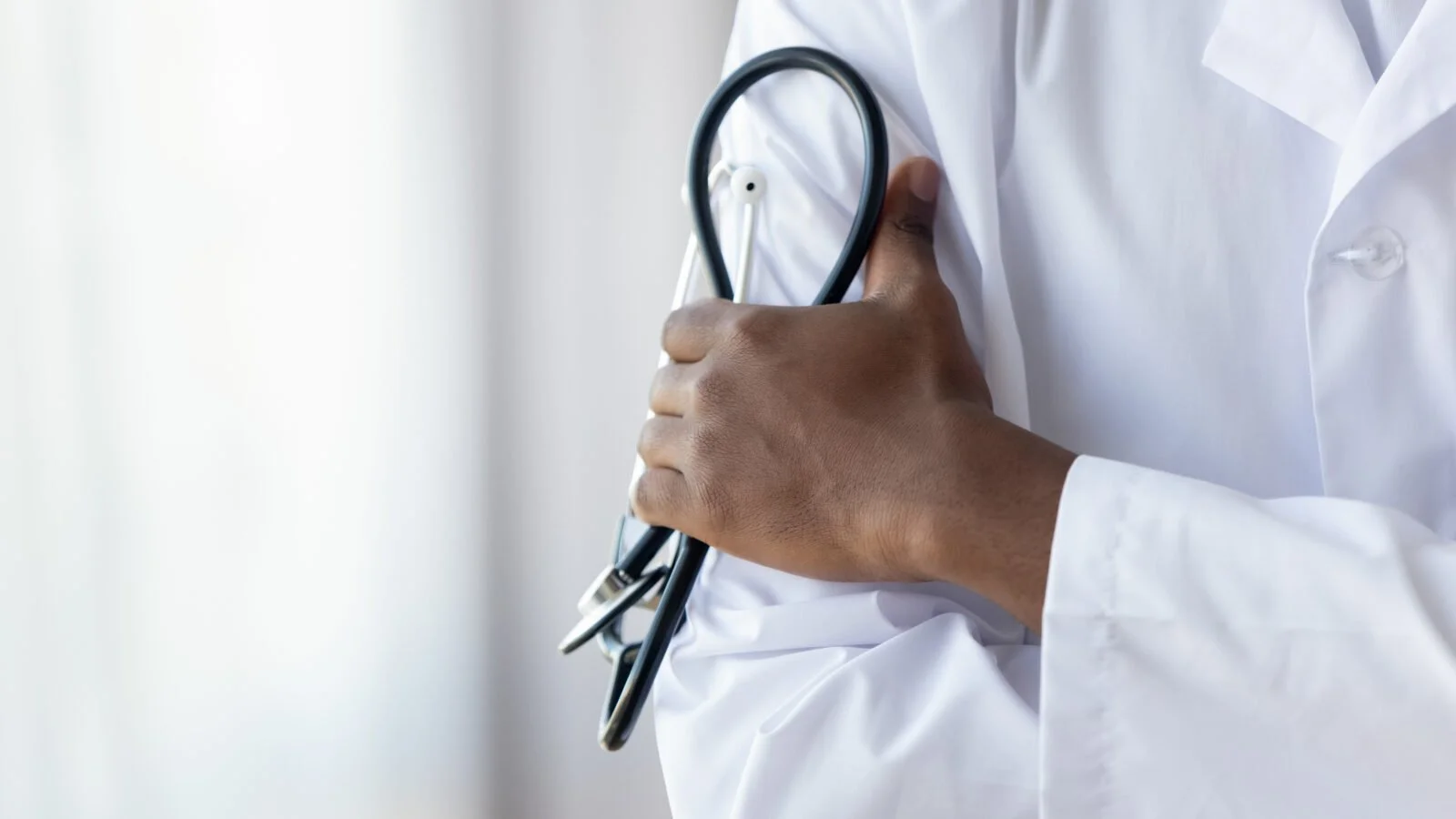 A doctor in a white coat holds a stethoscope against their chest.