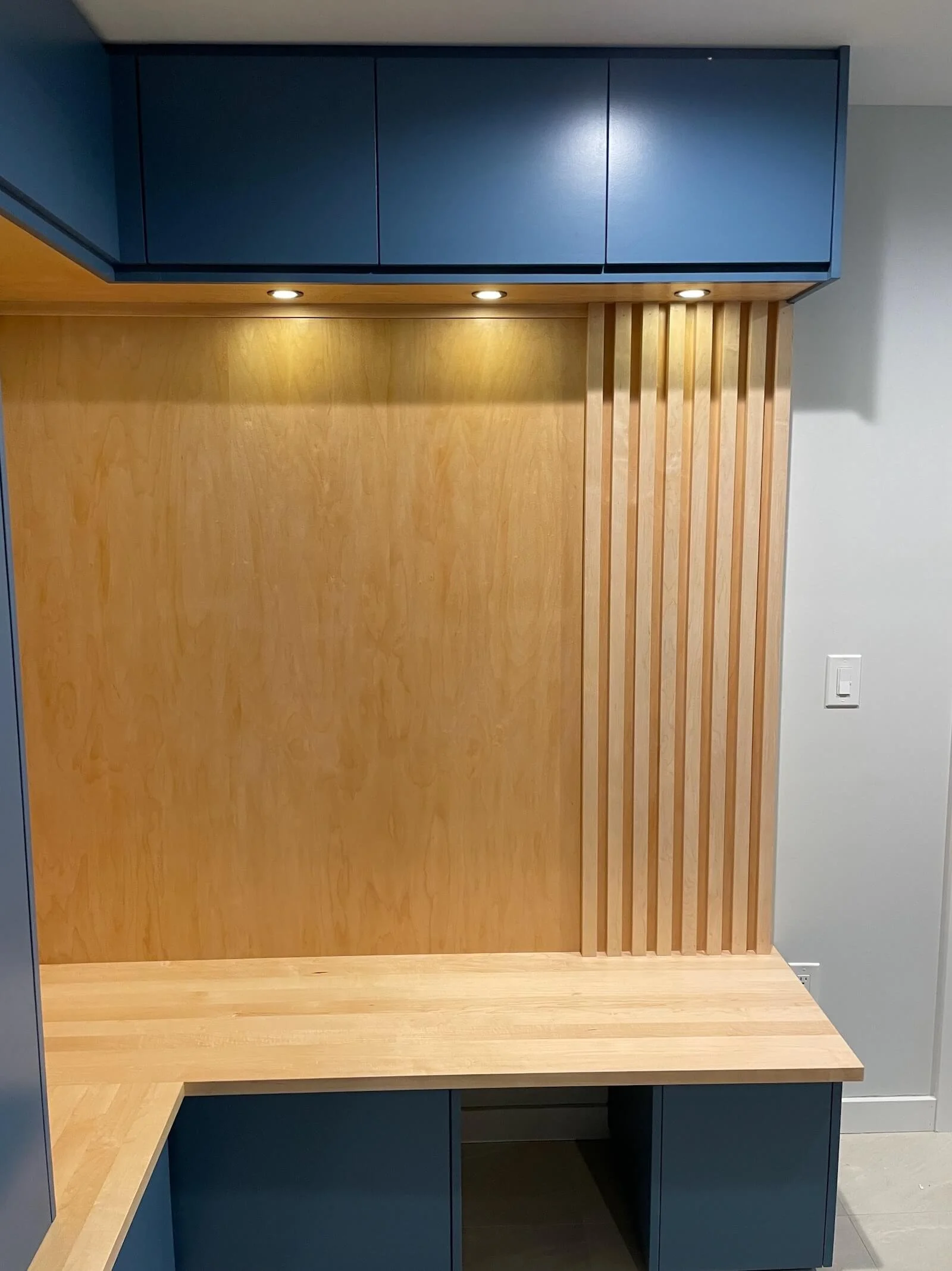 Custom mudroom cabinets with storage for shoes and coats with built-in lighting and slats, maple bench