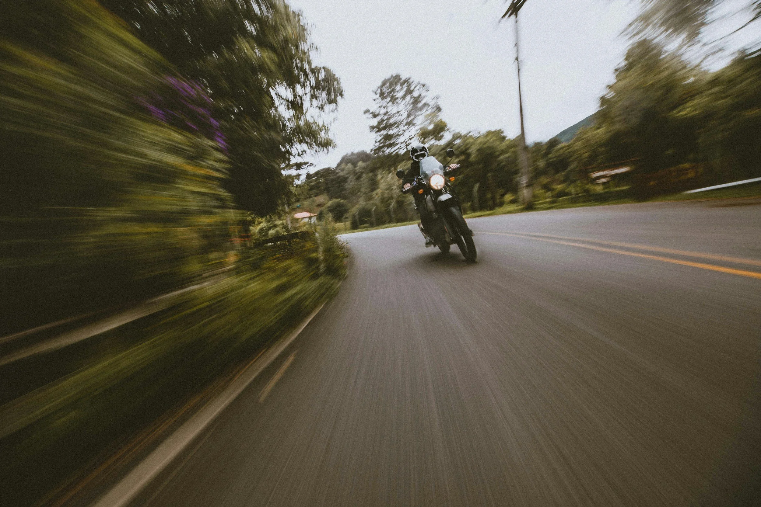 A person riding a motorcycle on a winding road with trees and power lines on the sides, captured during motion