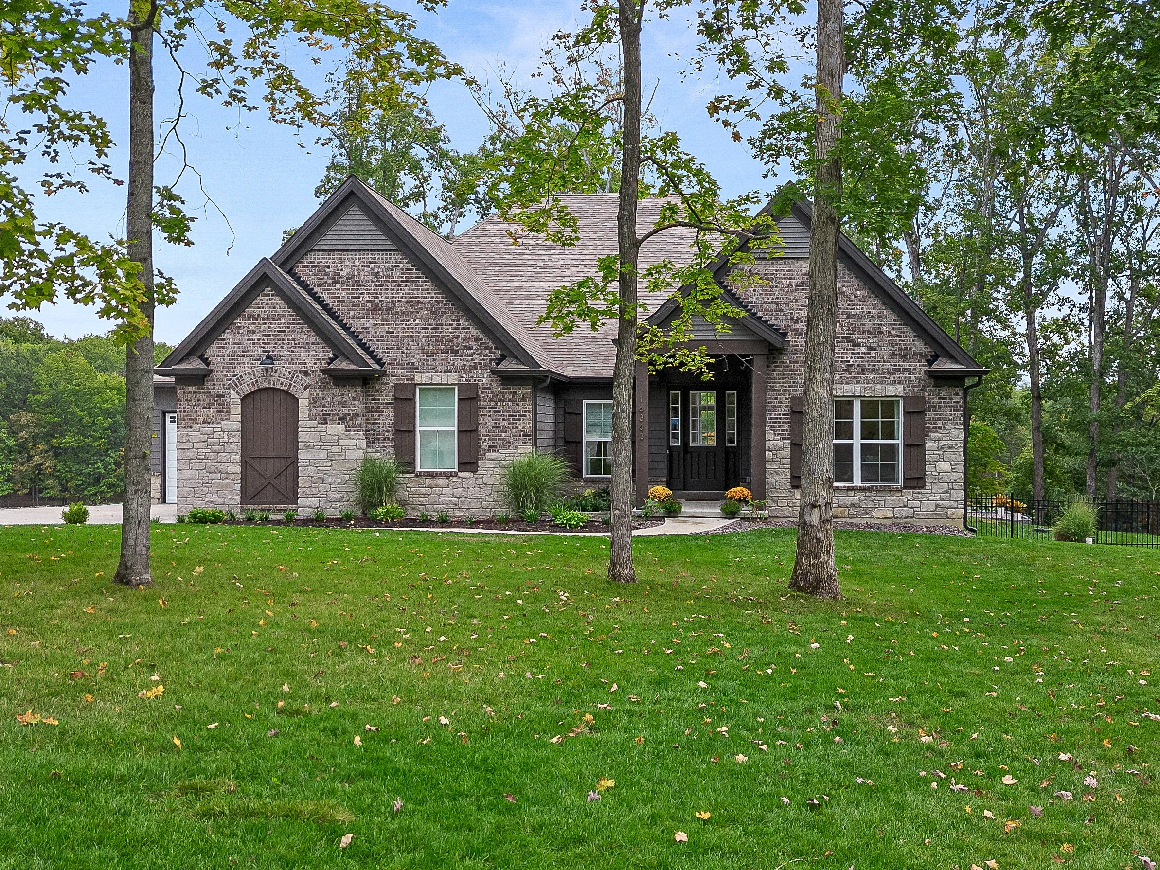 A brick and stone house with a front porch and black door, surrounded by a green lawn and trees.