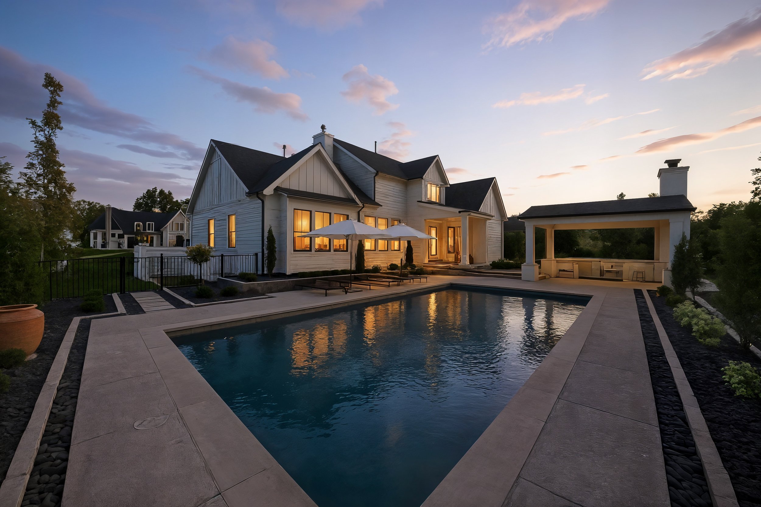 A house with large windows and a backyard swimming pool during sunset, with outdoor seating and umbrellas.