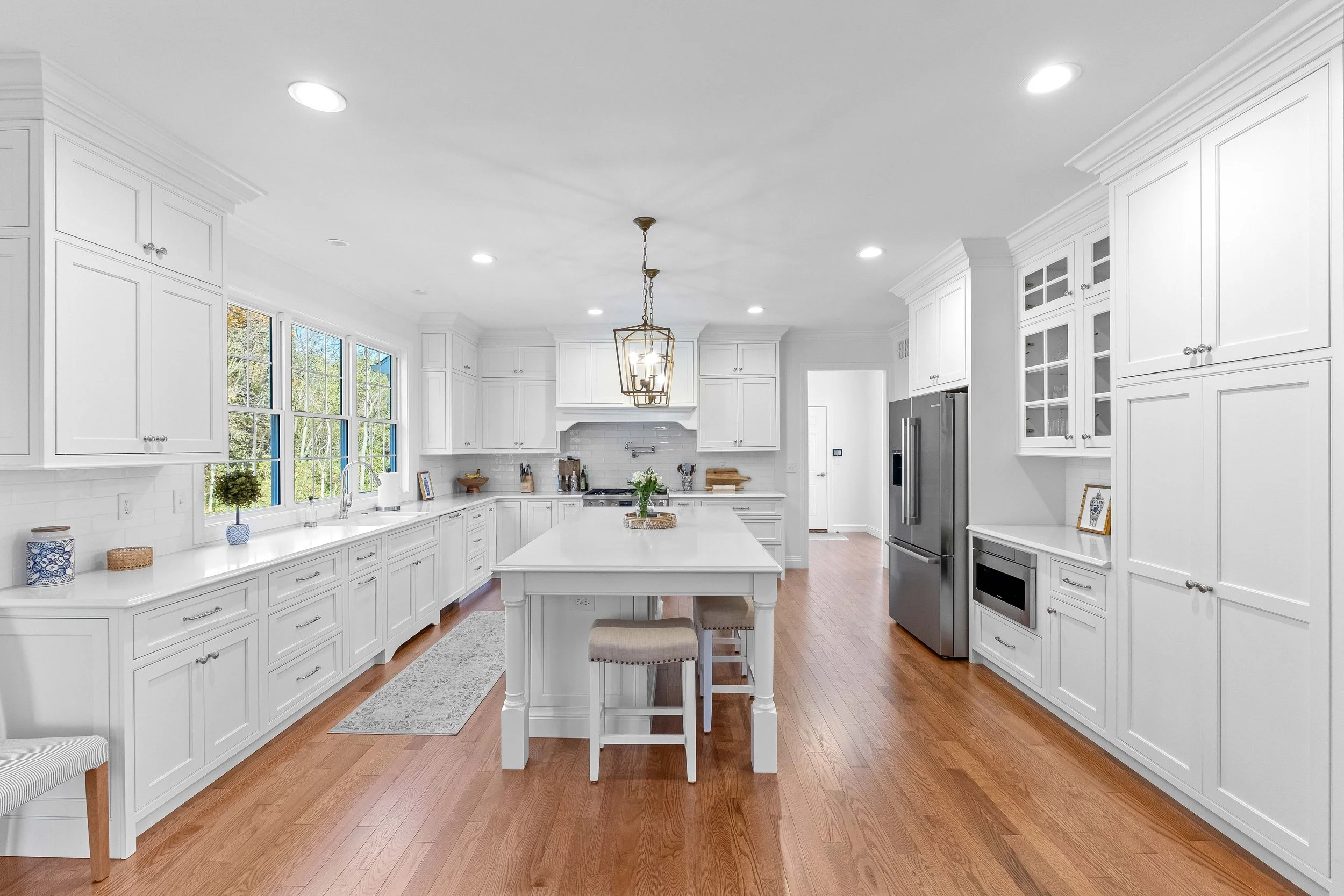 Bright kitchen with white cabinets, a large island, wood flooring, and stainless steel appliances.