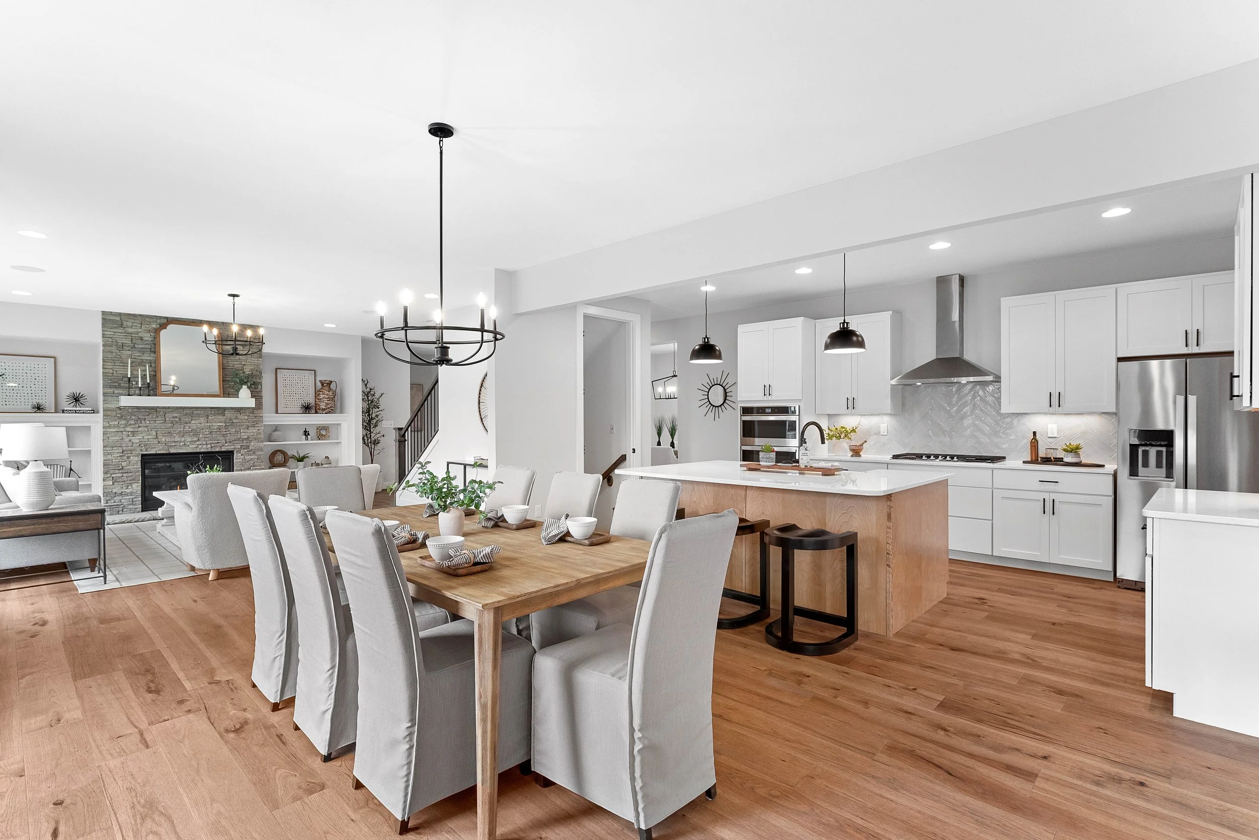 Open-concept kitchen and dining room with white cabinets, wooden island, stainless steel appliances, and a large wooden dining table with beige chairs.