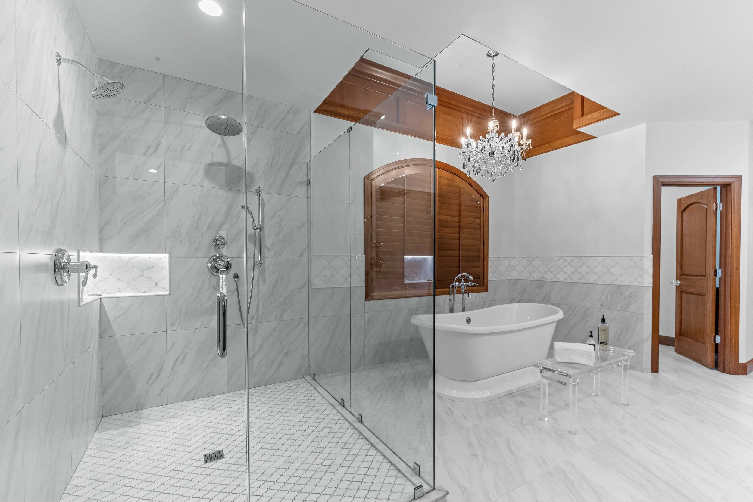 Luxurious bathroom with a spacious walk-in shower, freestanding bathtub, chandelier, and wooden accents.