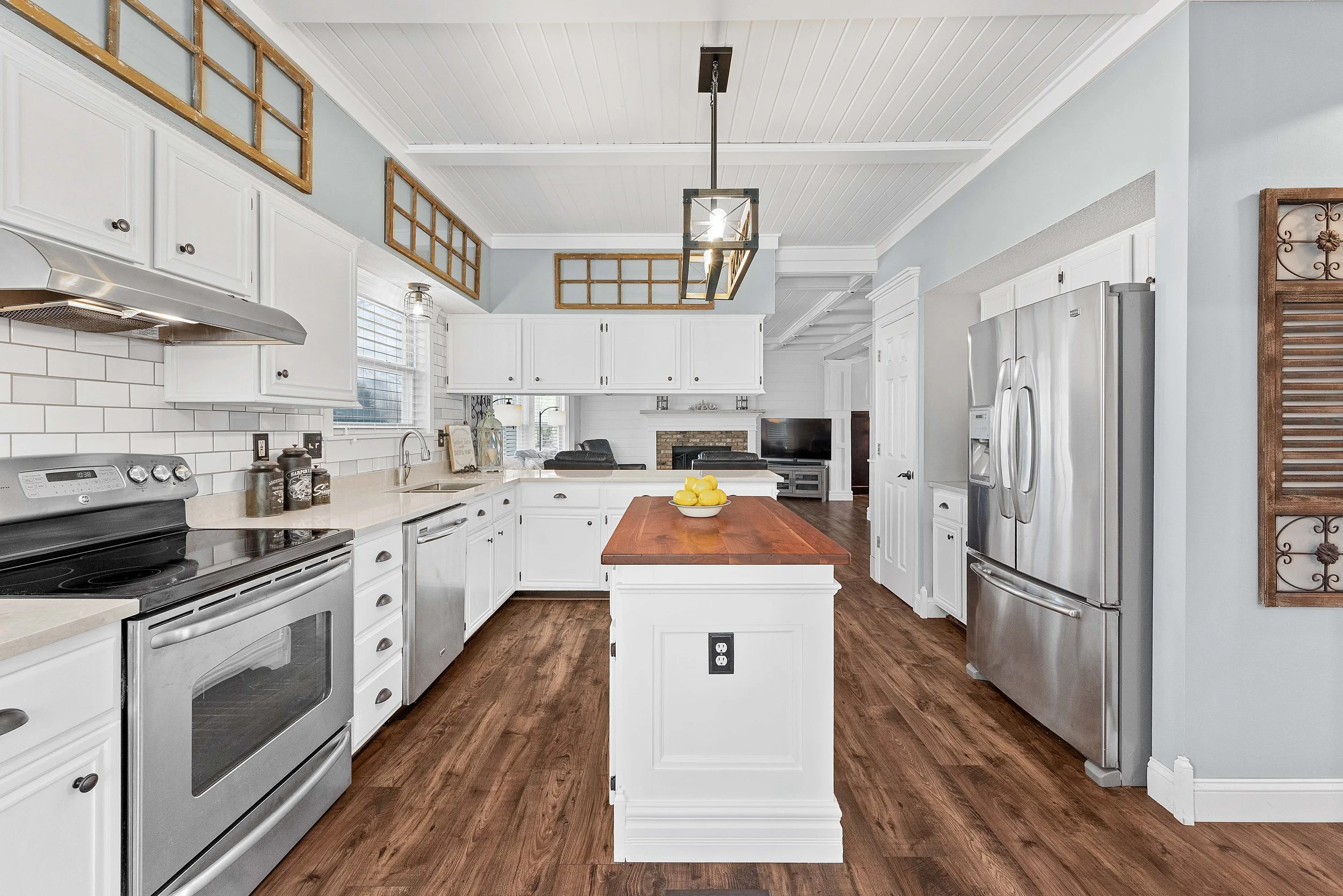 Bright kitchen with white cabinets, stainless steel appliances, wooden flooring, and a kitchen island with lemon bowl.