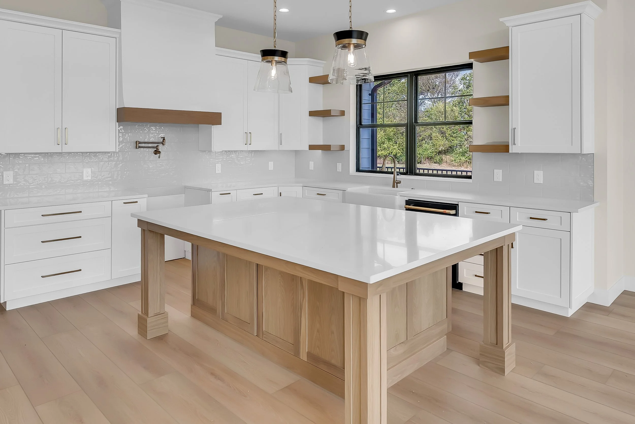 Bright, modern kitchen with white cabinets, a large central island with a wooden base, hardwood floors, a window over the sink, and pendant lights hanging above the island.