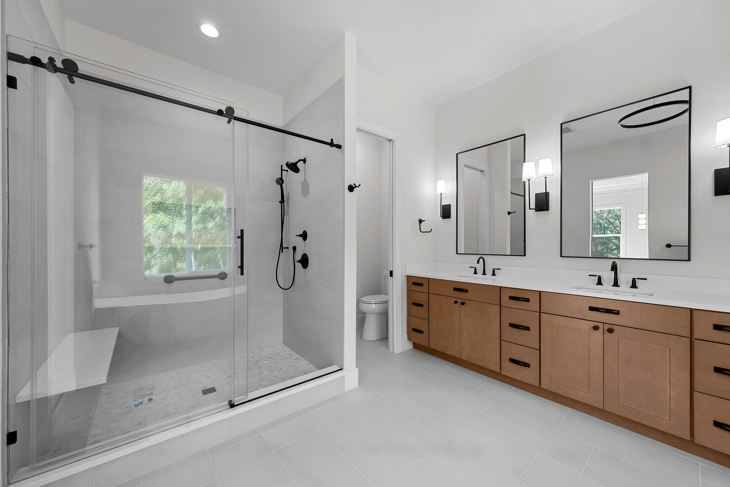 Modern bathroom with walk-in shower, double vanity with mirrors, and wooden cabinetry.