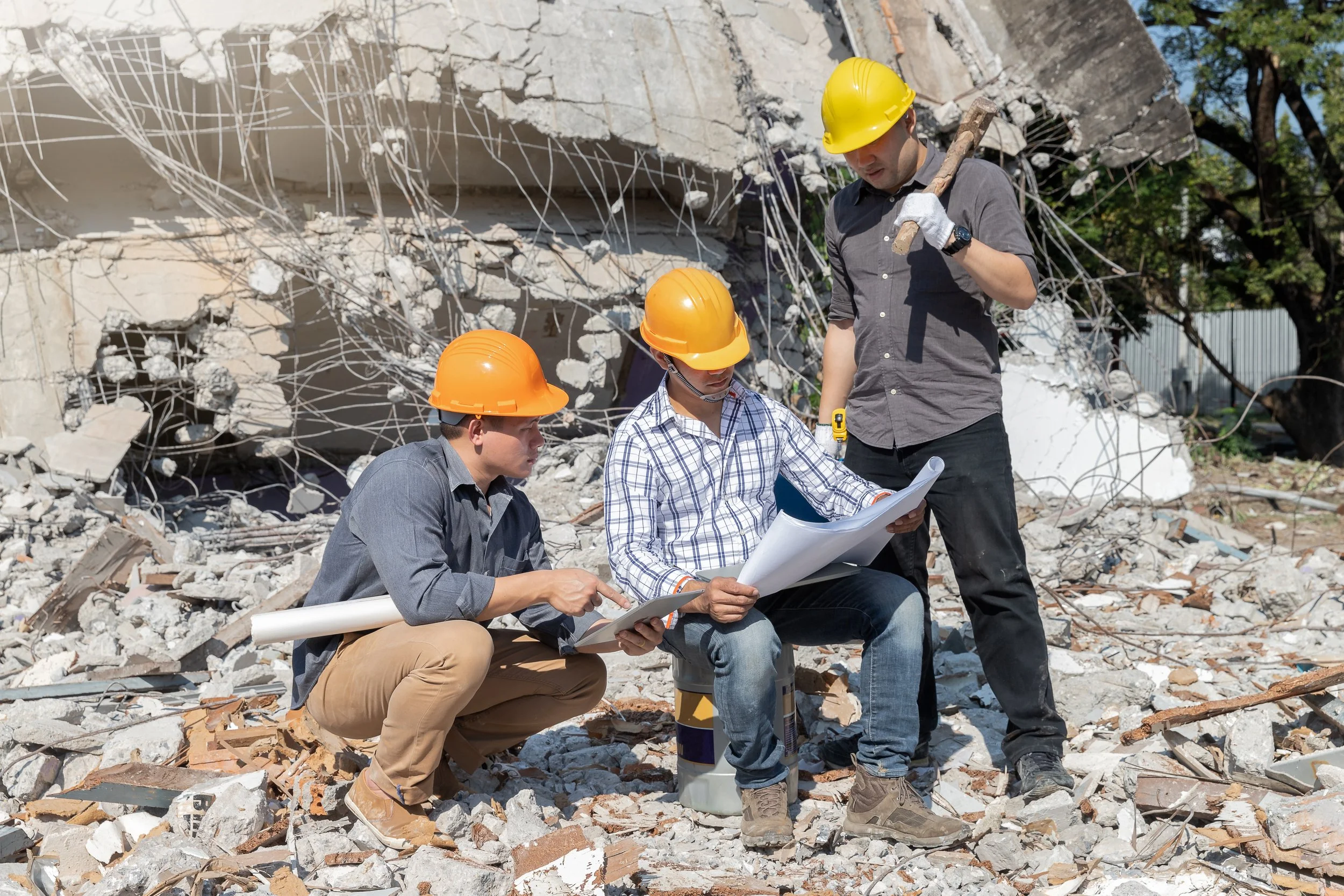Construction workers wearing helmets reviewing plans at a building collapse site with debris and broken concrete