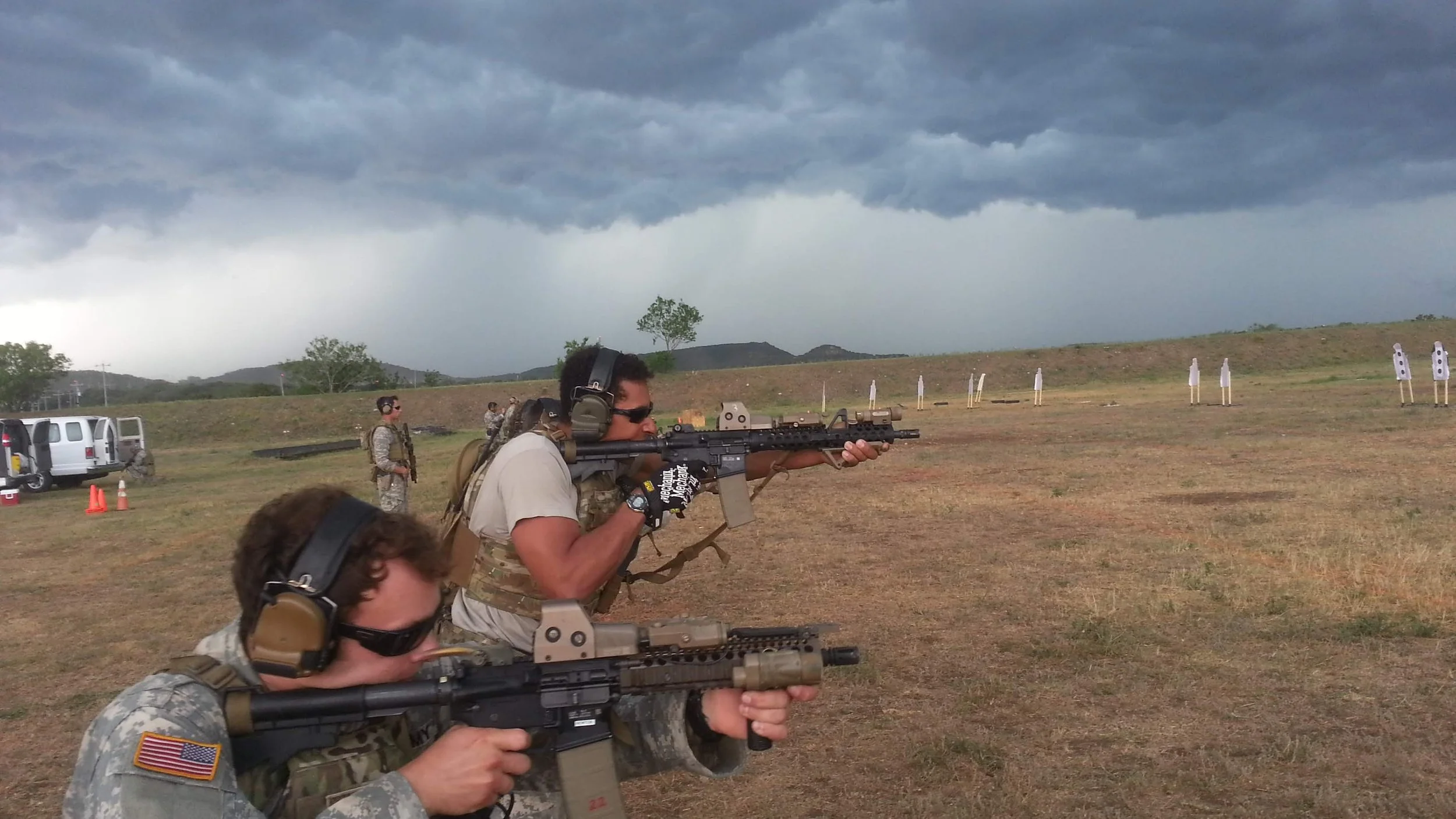 Two soldiers aiming rifles during a shooting practice on an open field under a cloudy sky.