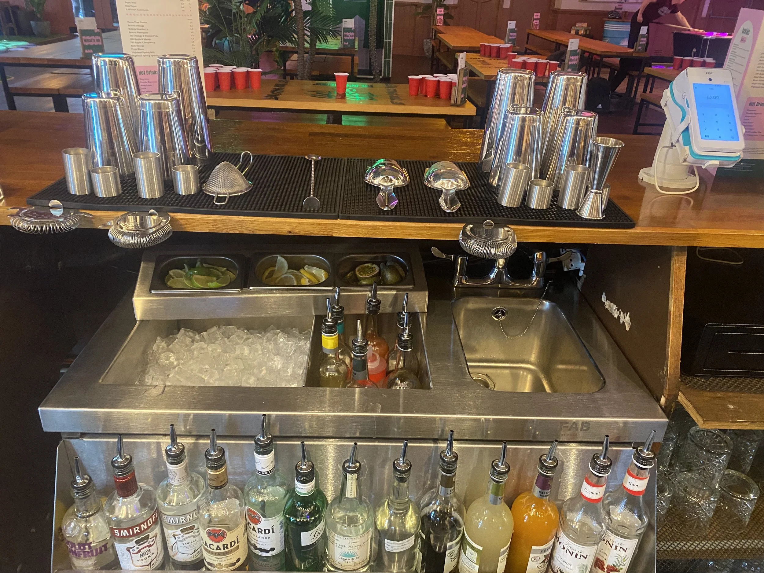 Bar setup with bottles of liquor, ice, and bar tools, along with shot glasses and cocktail ingredients.