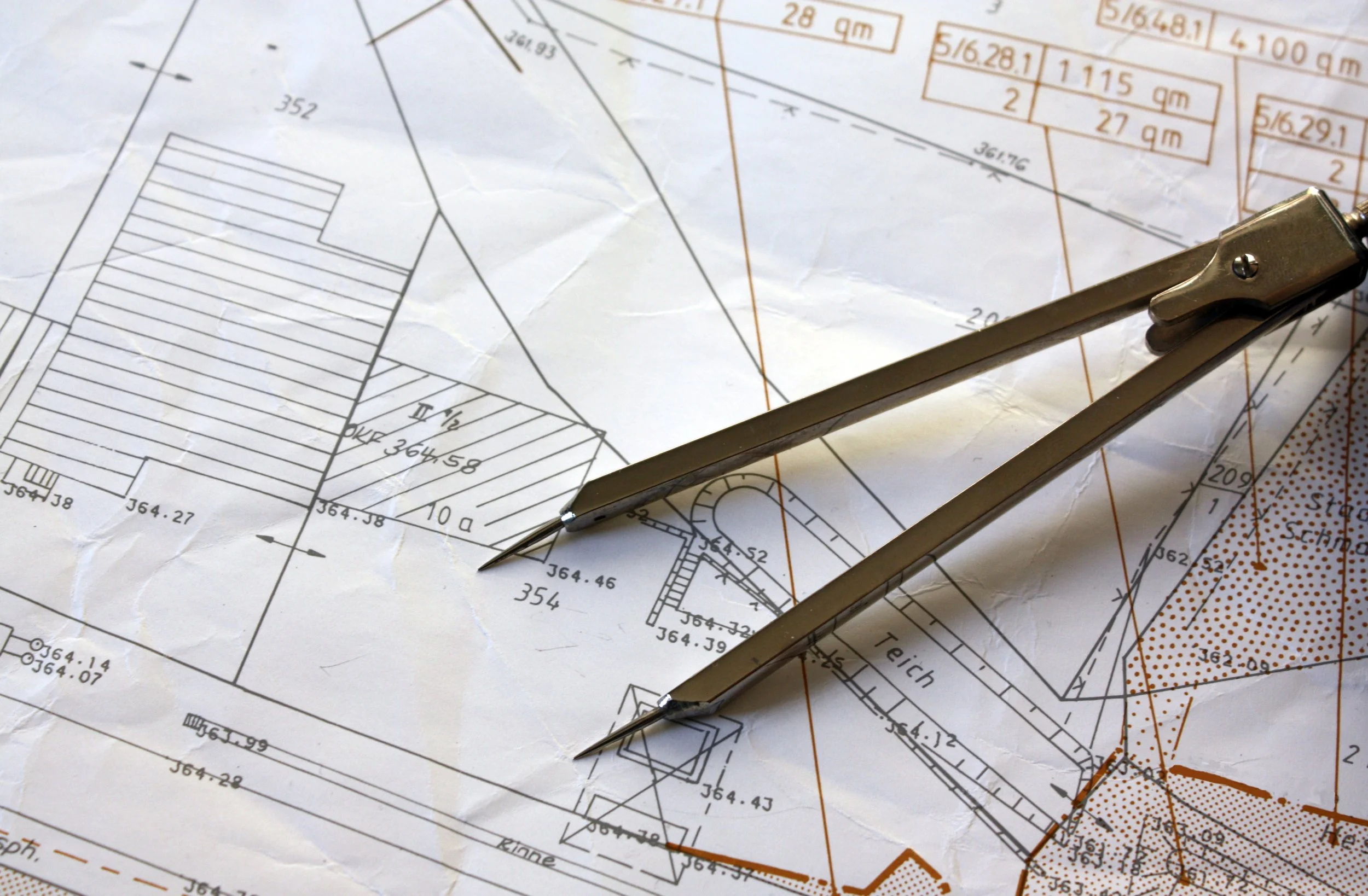 Blueprints or architectural plans with a pair of compasses on top.