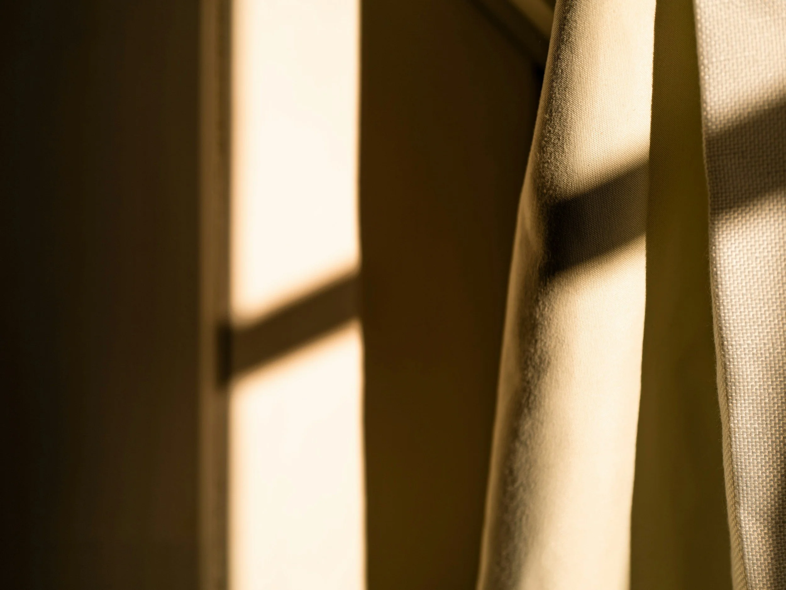 Sunlight casting shadows through a window onto beige curtains.