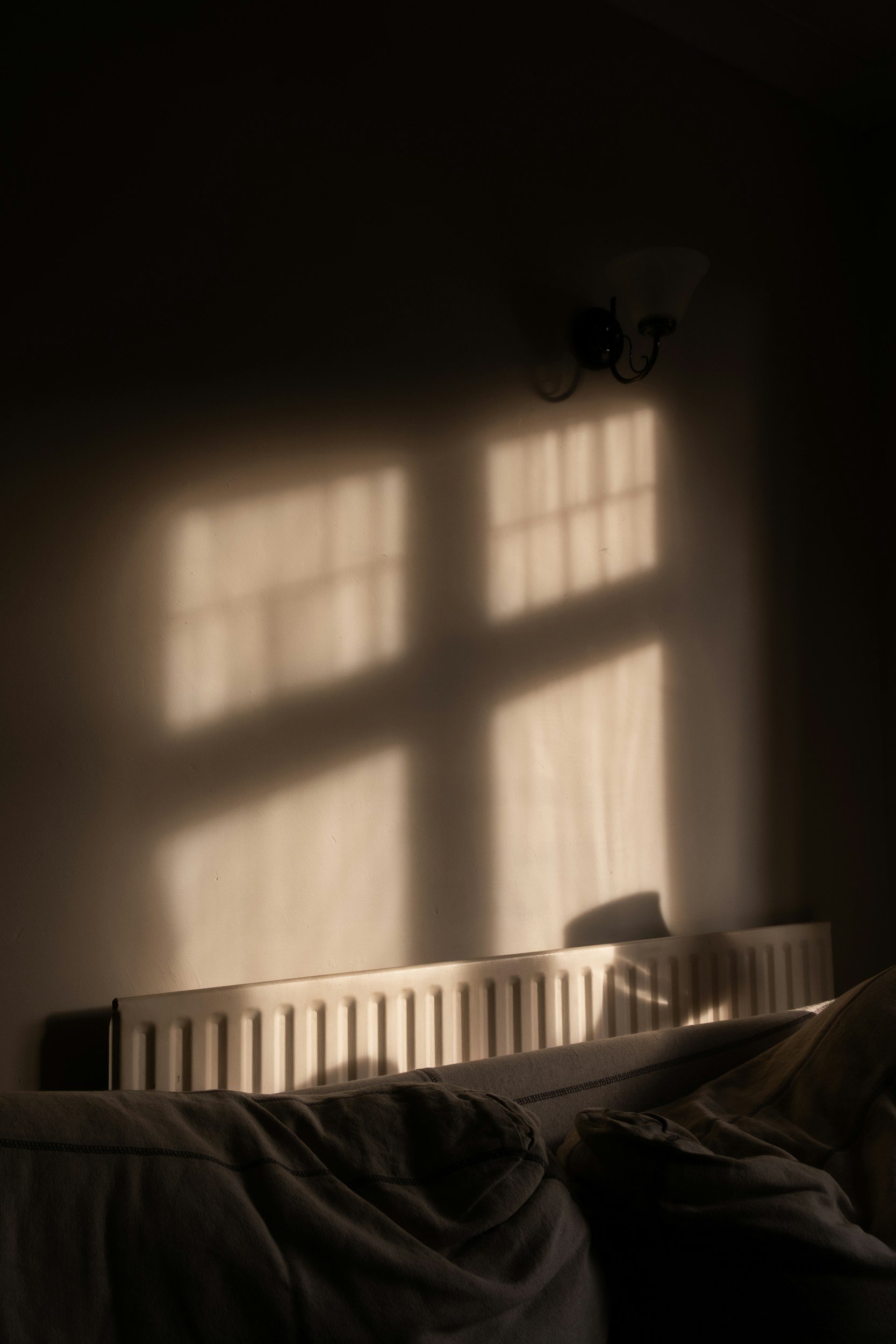 Sunlight casting a window cross shadow on a wall in a dimly lit room