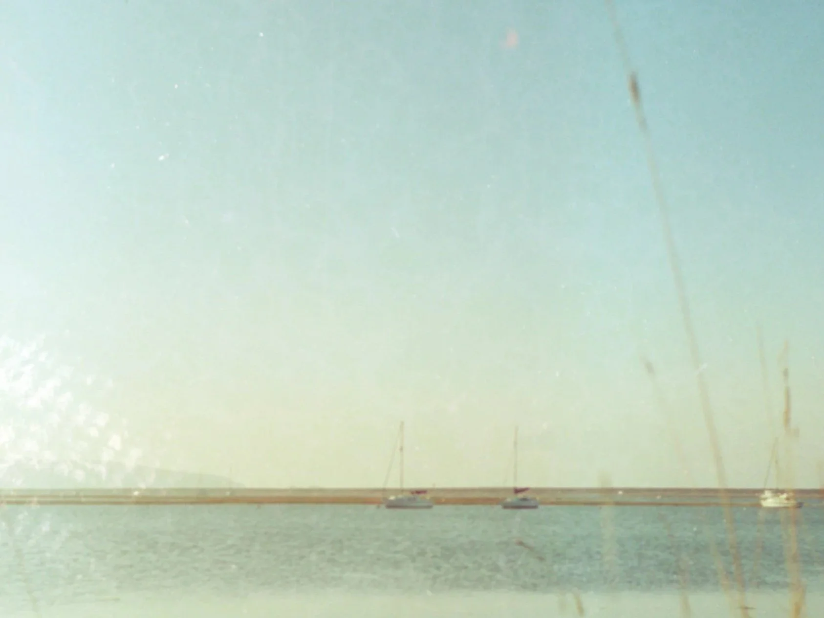 A hazy view of water with two sailboats and a bridge in the distance, viewed from a foggy or dirty window.