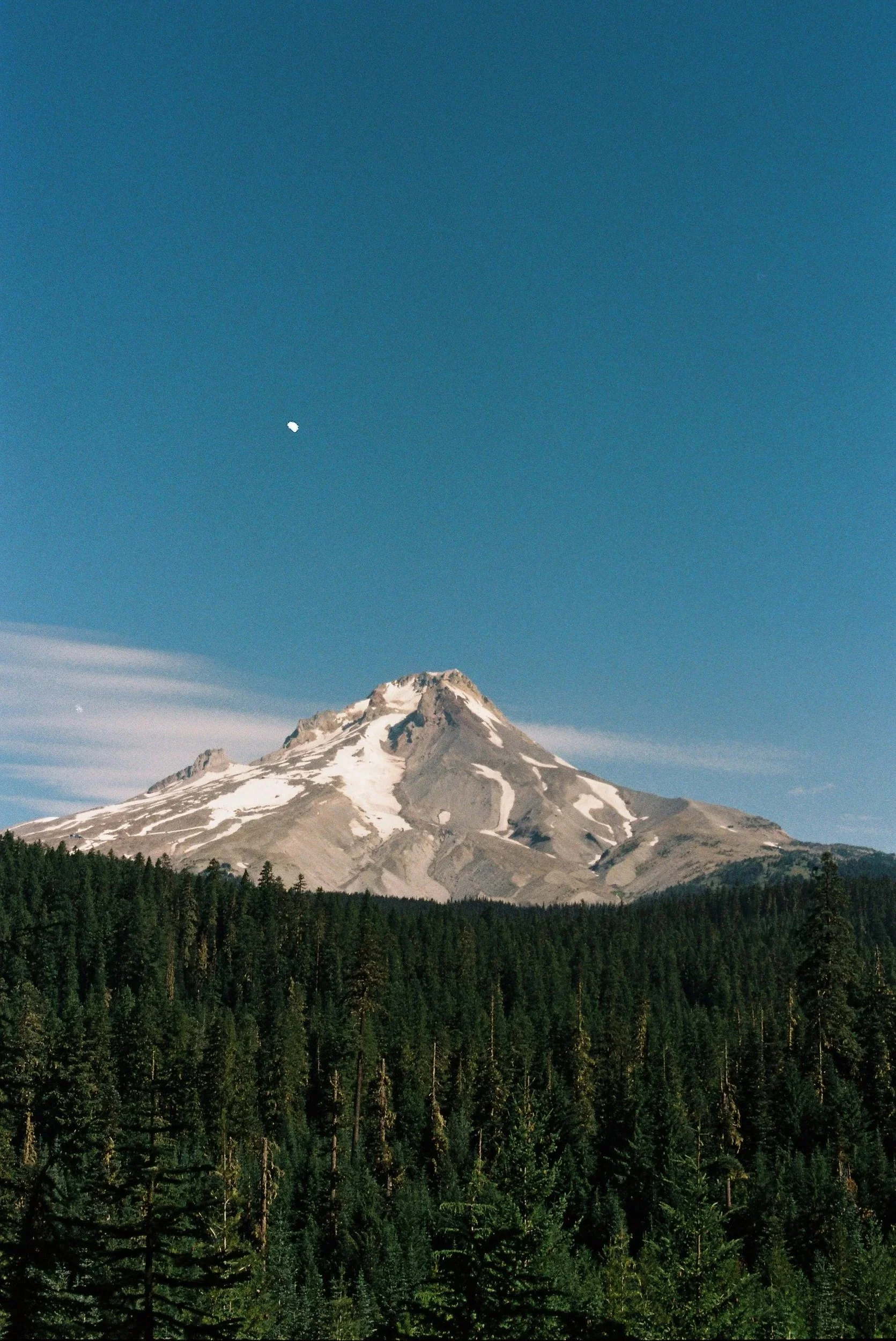 A snow-capped mountain under a clear blue sky with a visible moon.