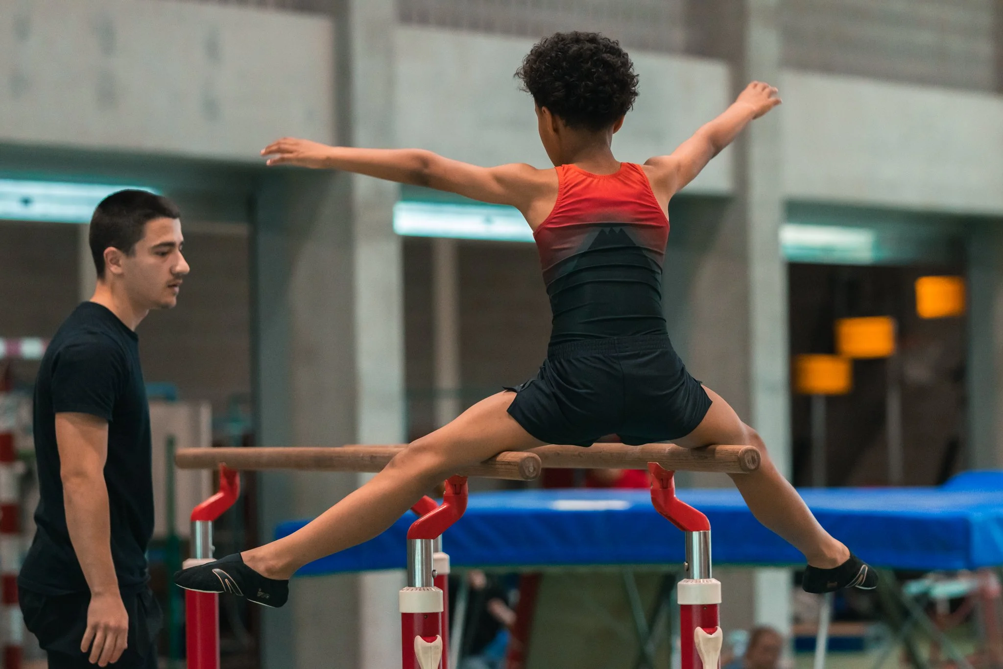 Une jeune fille effectue une figure de gymnastique au sol sur une poutre avec un entraîneur à côté dans une salle de gymnastique.