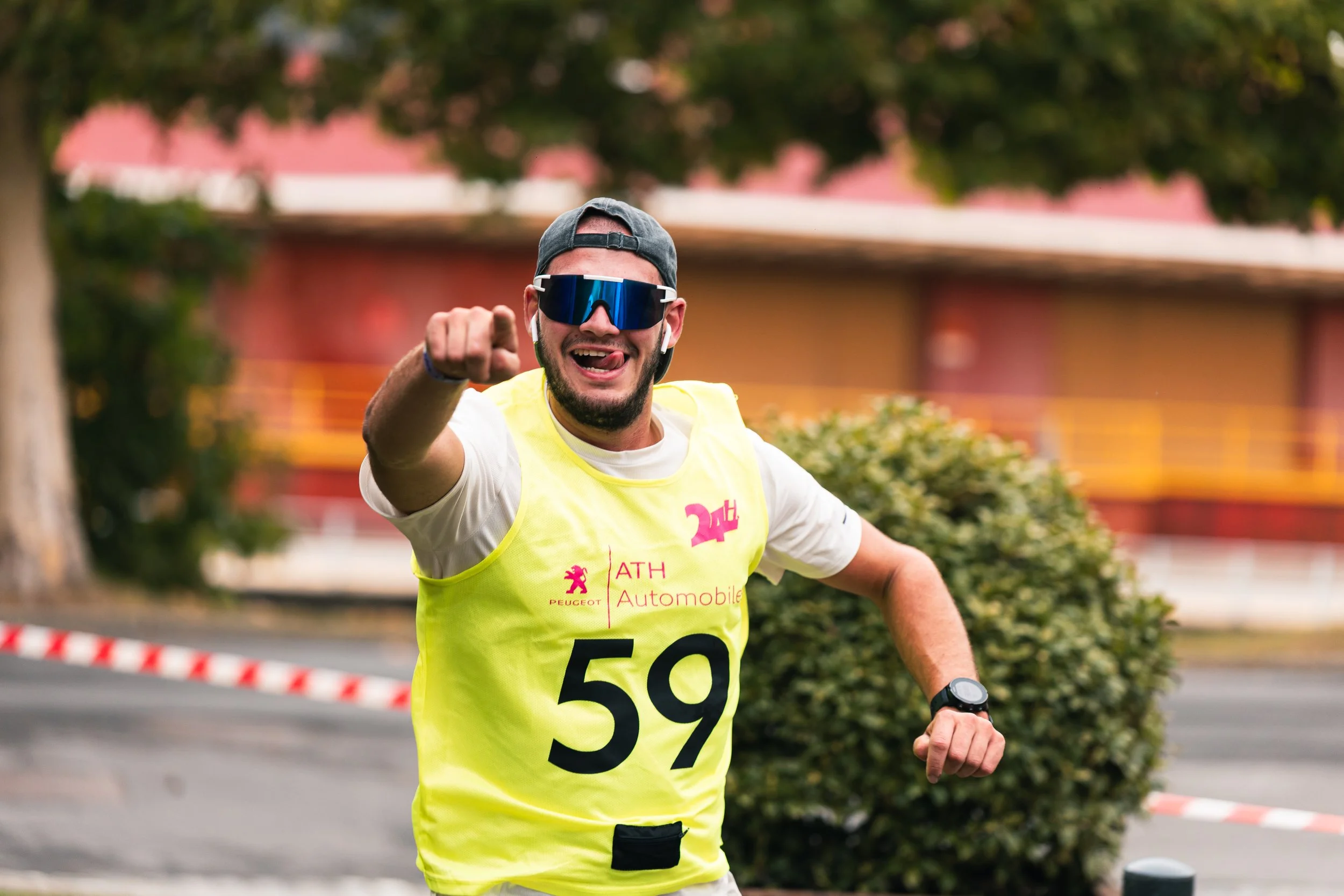 Un homme en tenue de course, portant une veste fluo avec le numéro 59, sourit et fait un geste de la main lors d'une course