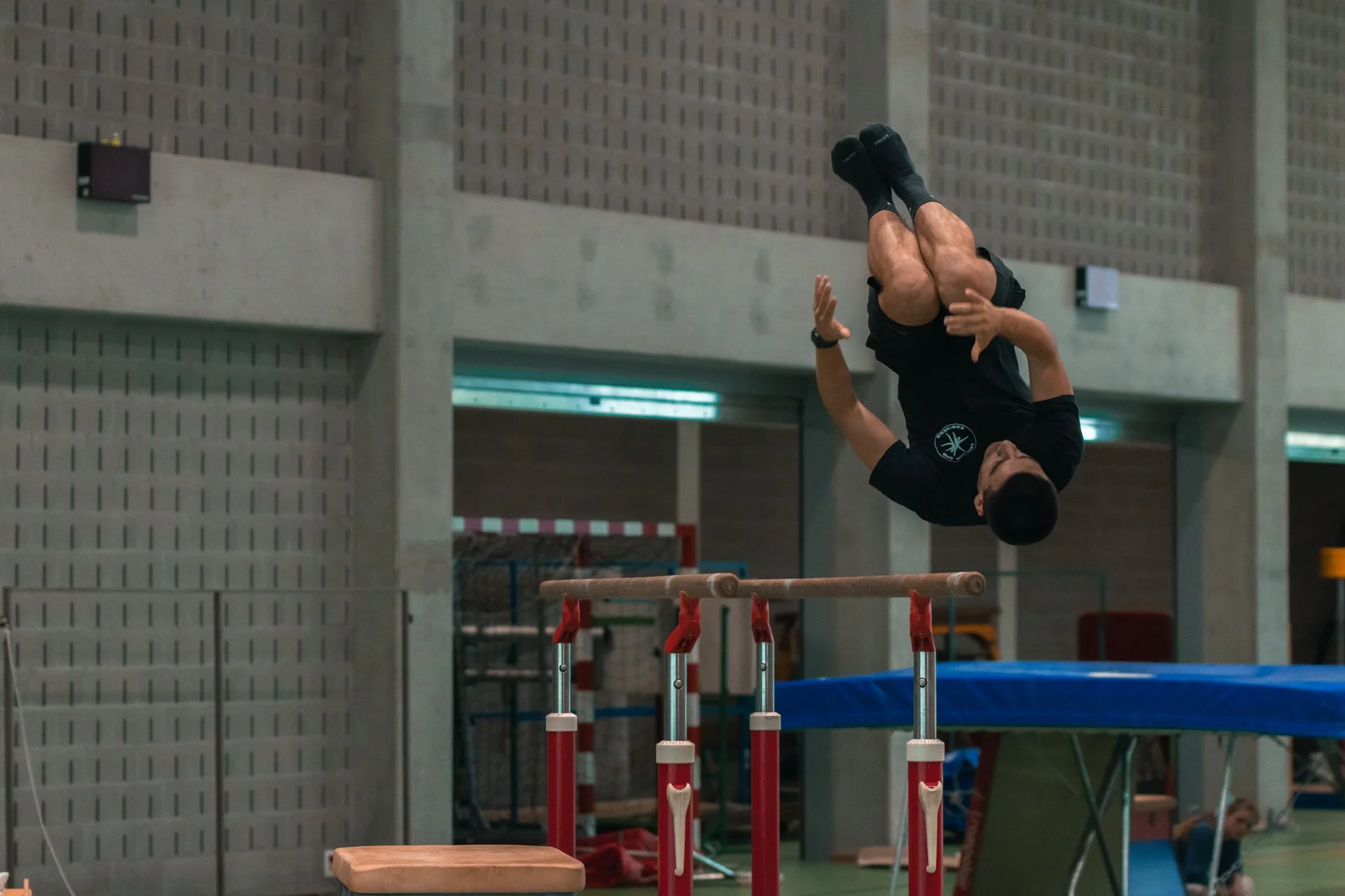 Un homme effectue un saut dans une salle d'entraînement, en faisant du saut à la barre fixée à une structure métallique, avec un trampoline en dessous.