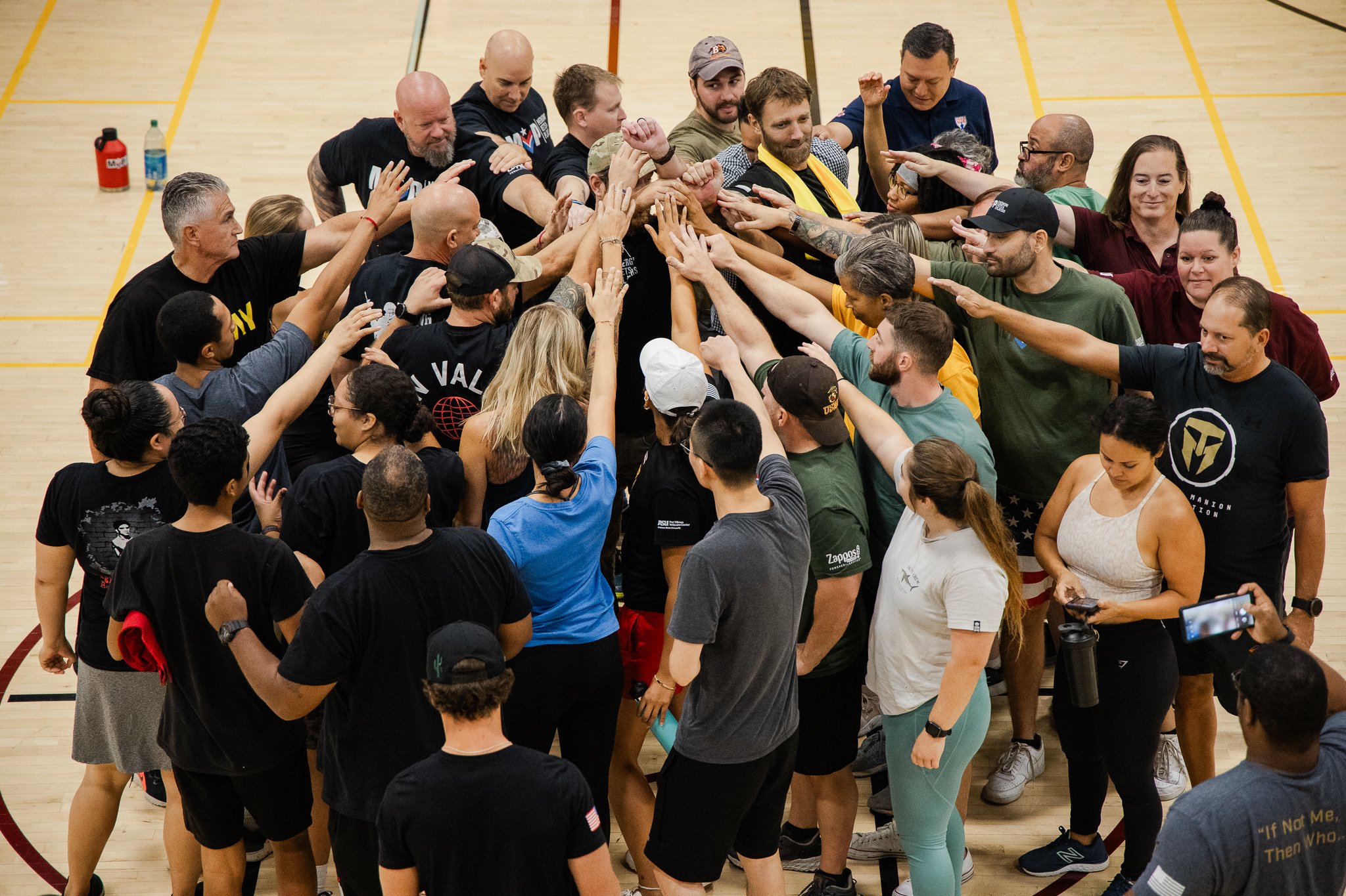 Group of people in a gymnasium forming a human chain, reaching out and touching hands towards the center.