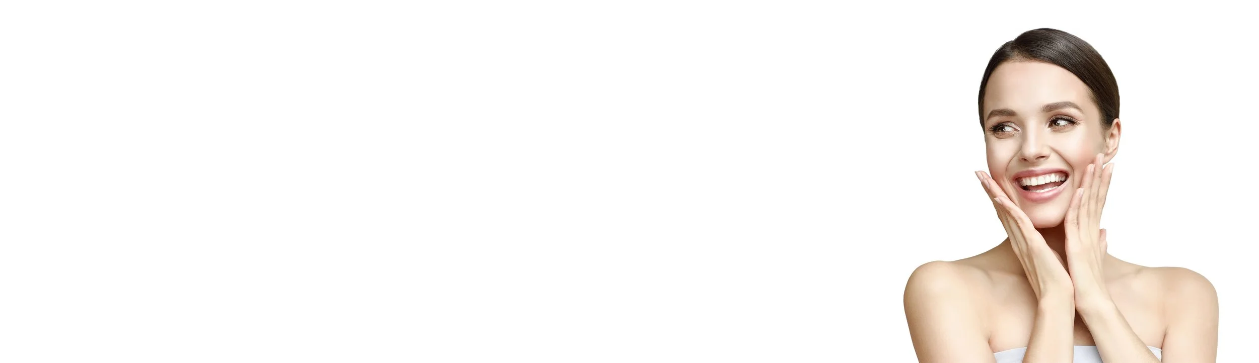 A young woman with clear skin smiling with her hands gently touching her cheeks, looking to the side, against a white background.