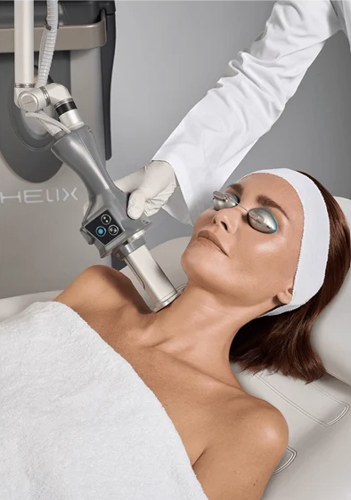 A woman lying down with protective eye shields, receiving a cosmetic treatment from a professional using a laser device.
