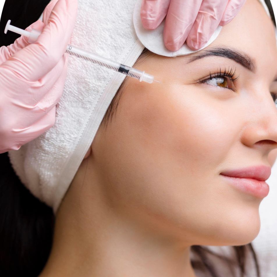 A woman with a headband receiving a cosmetic injection near her eyebrow from a healthcare professional wearing pink gloves.