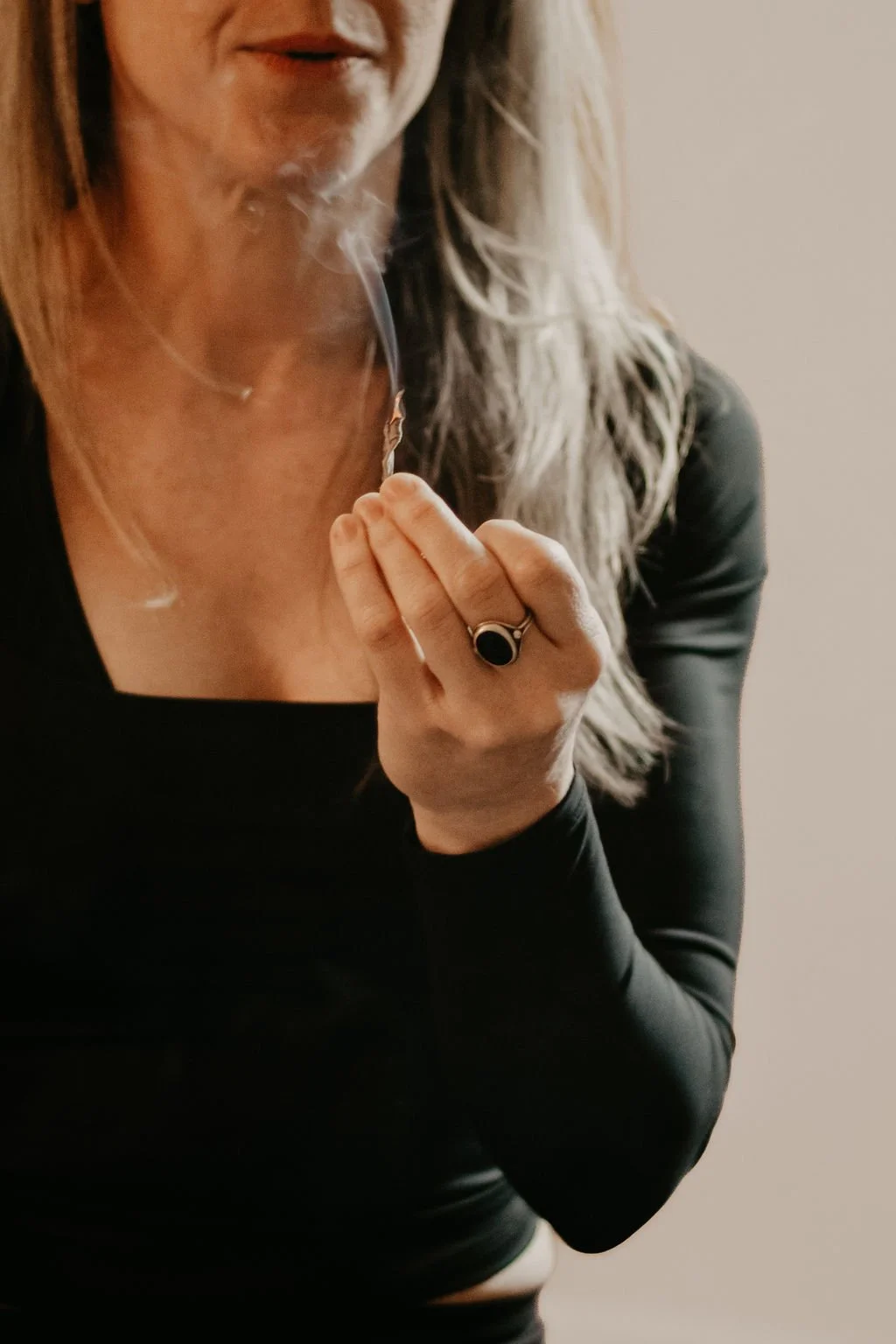 Woman holding a leaf of burning sage, smoke swirling toward the sky.