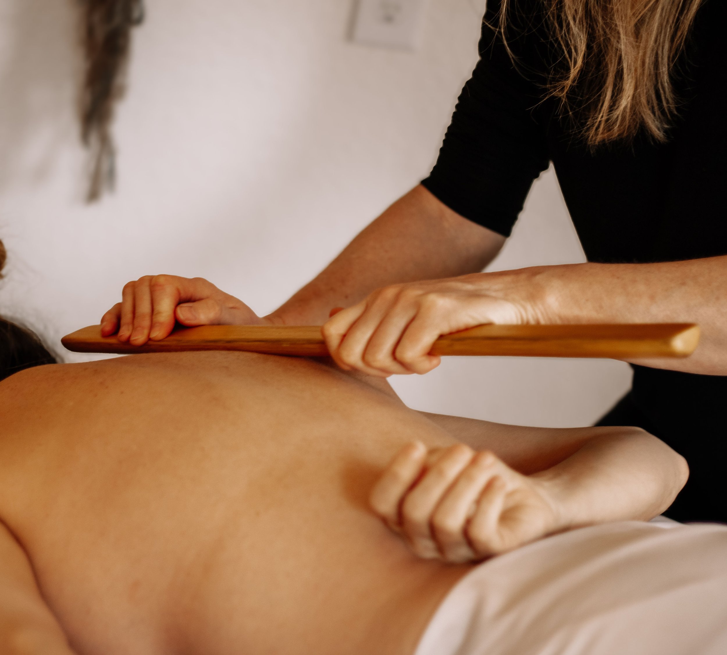 Massage therapist using a bamboo tool to provide treatment for a patient.