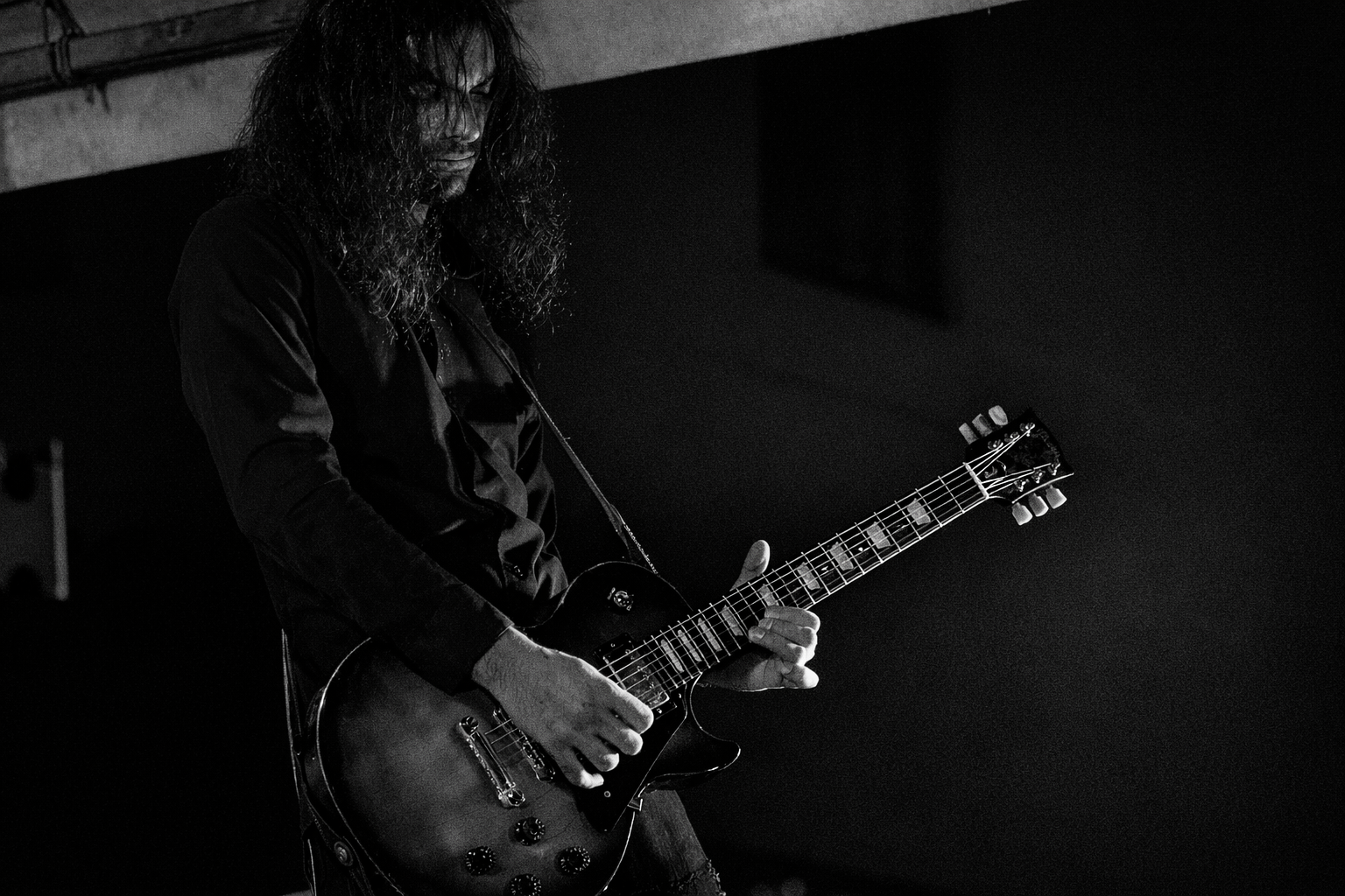 Black and white photo of a man with long, curly hair playing an electric guitar.