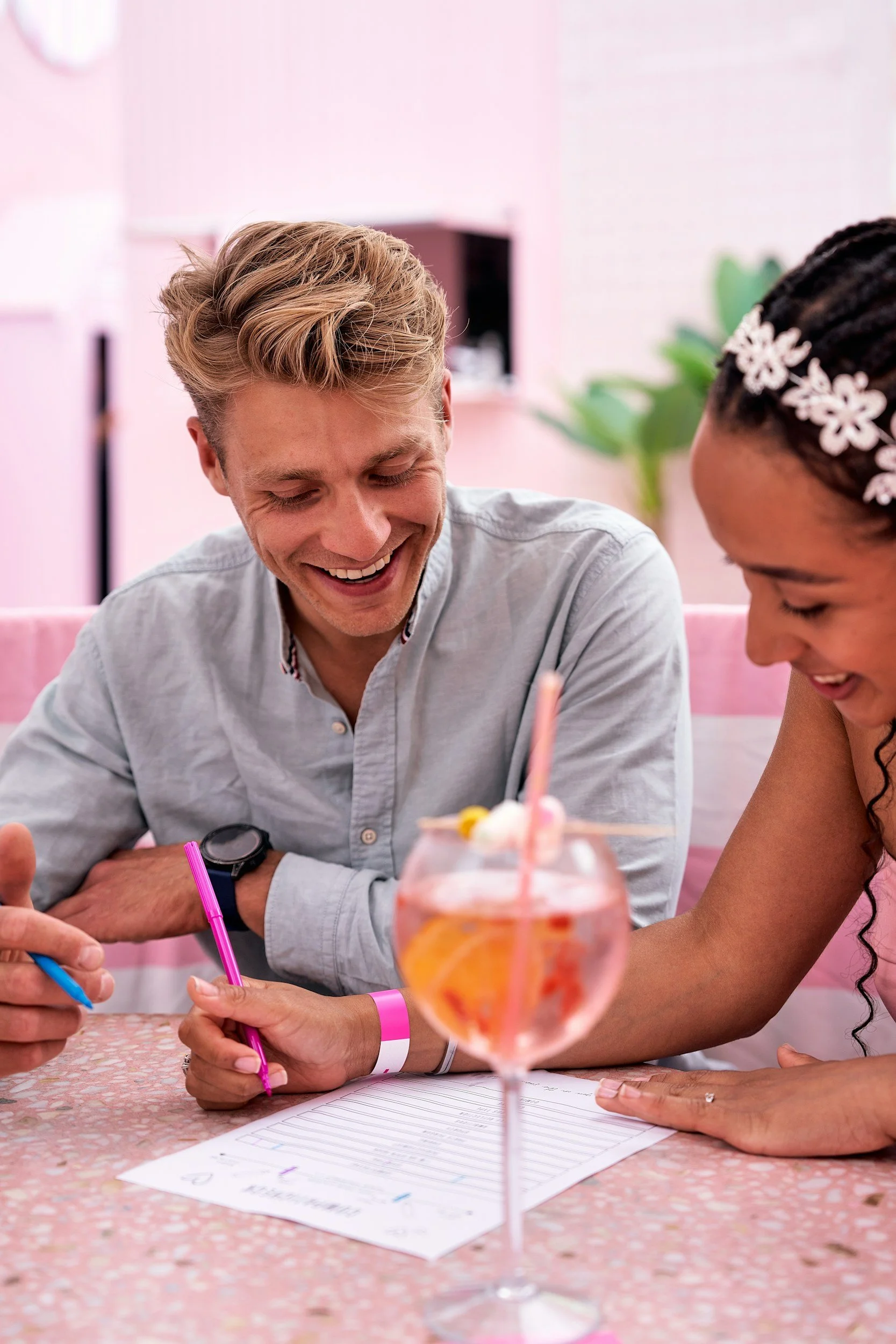 A man and woman are sitting at a table laughing and sipping wine while having fun doing art creative project together.