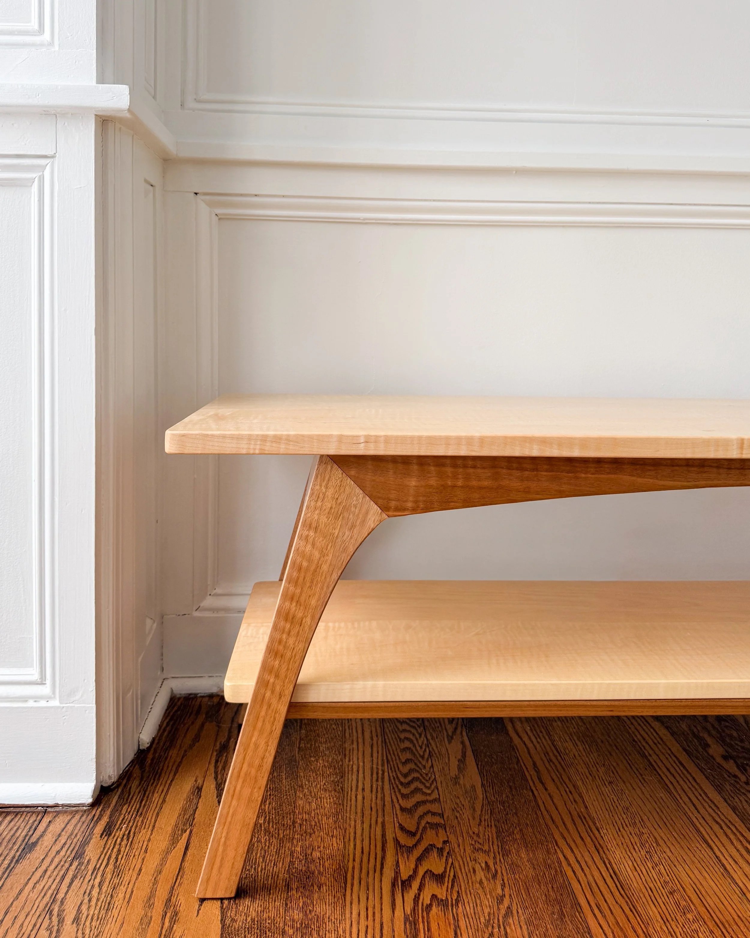 A modern wooden bookshelf with two shelves, placed against a white wall and on a hardwood floor.