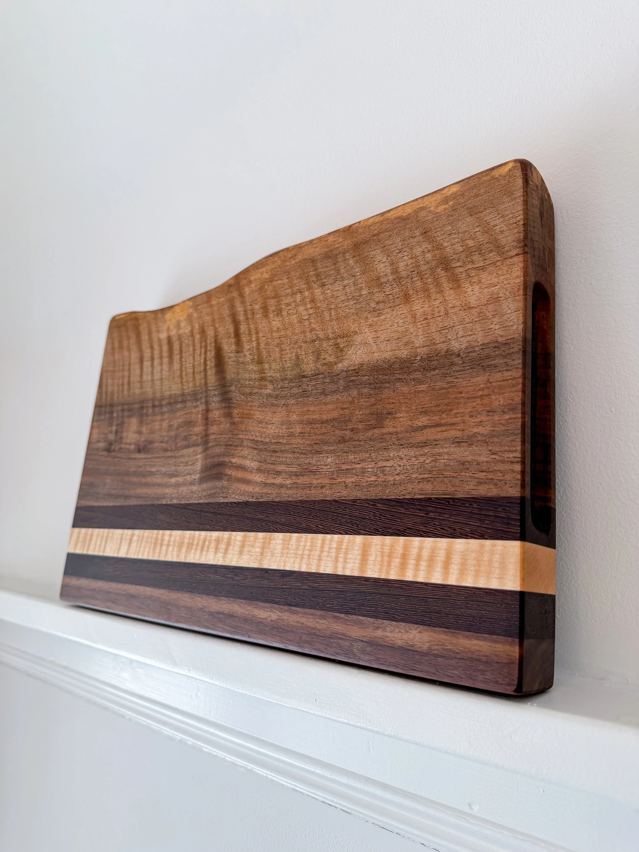Close-up of a rectangular wooden wall art piece with horizontal woodgrain patterns and multiple wood types, leaning against a white wall.