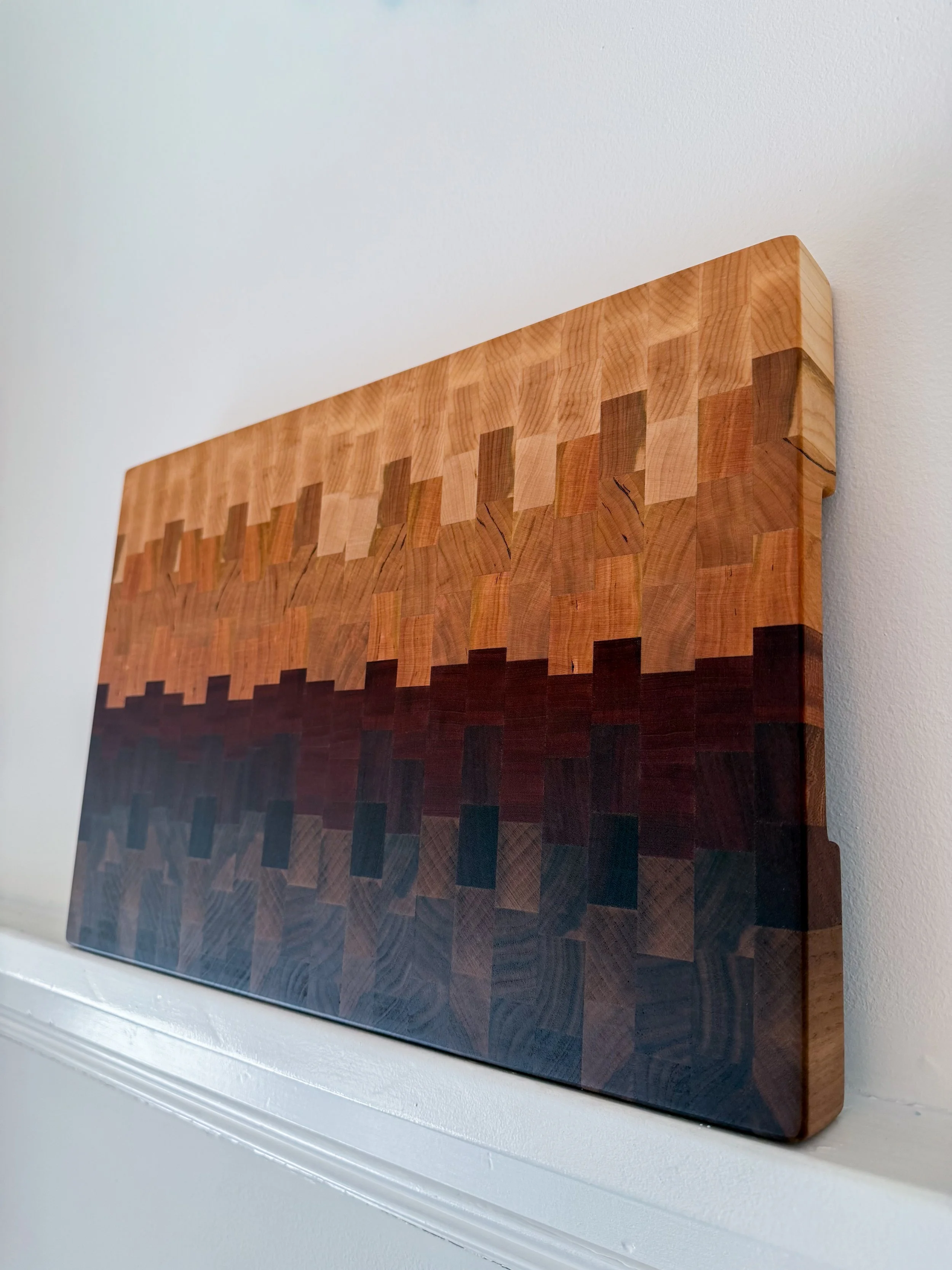 A wooden art piece with a geometric pattern made of squares and rectangles, showing variation in wood grain and colors from light to dark, mounted on a white wall.