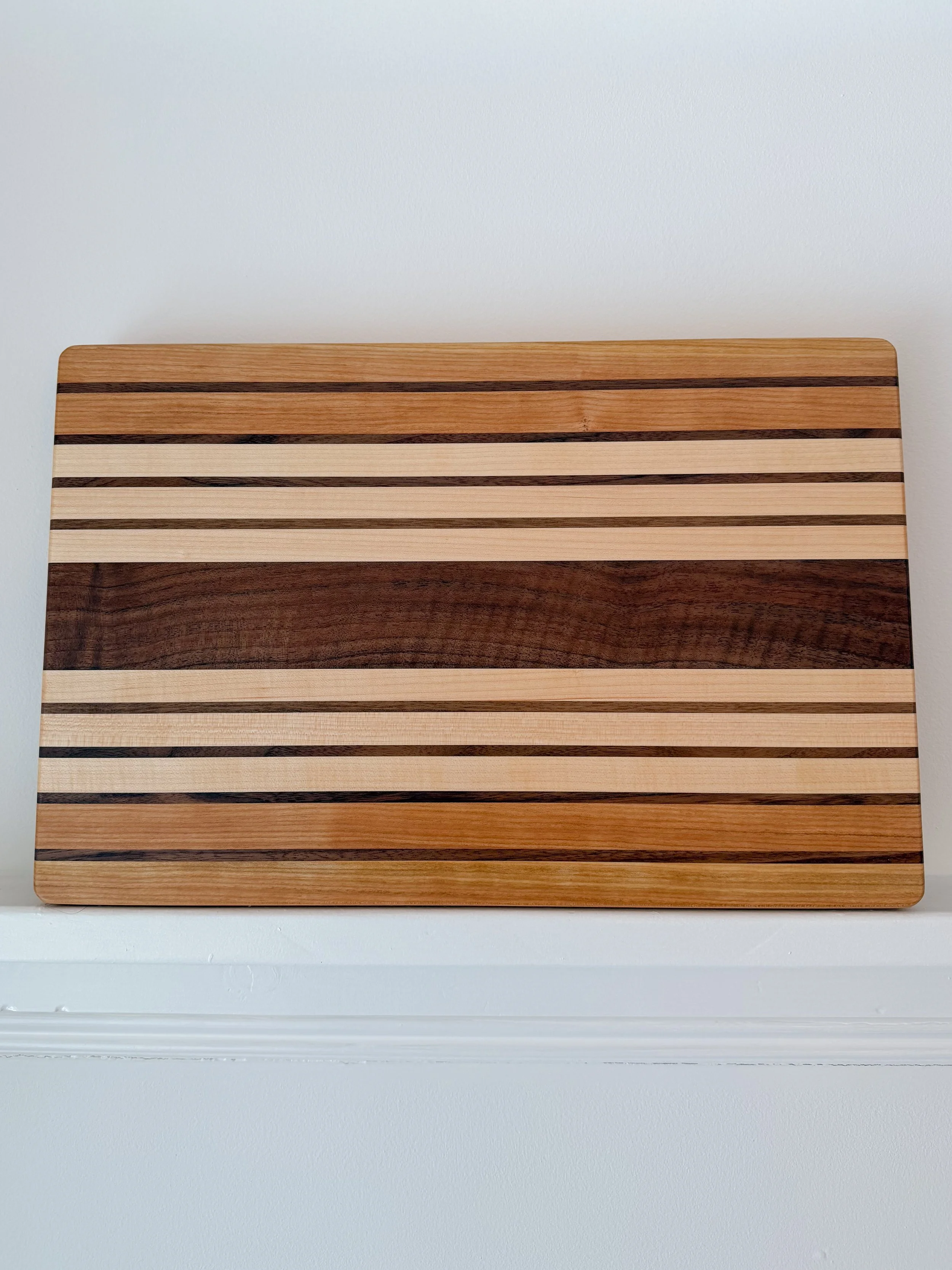 A rectangular wooden board with alternating light and dark wood stripes, placed on a white surface against a white wall background.
