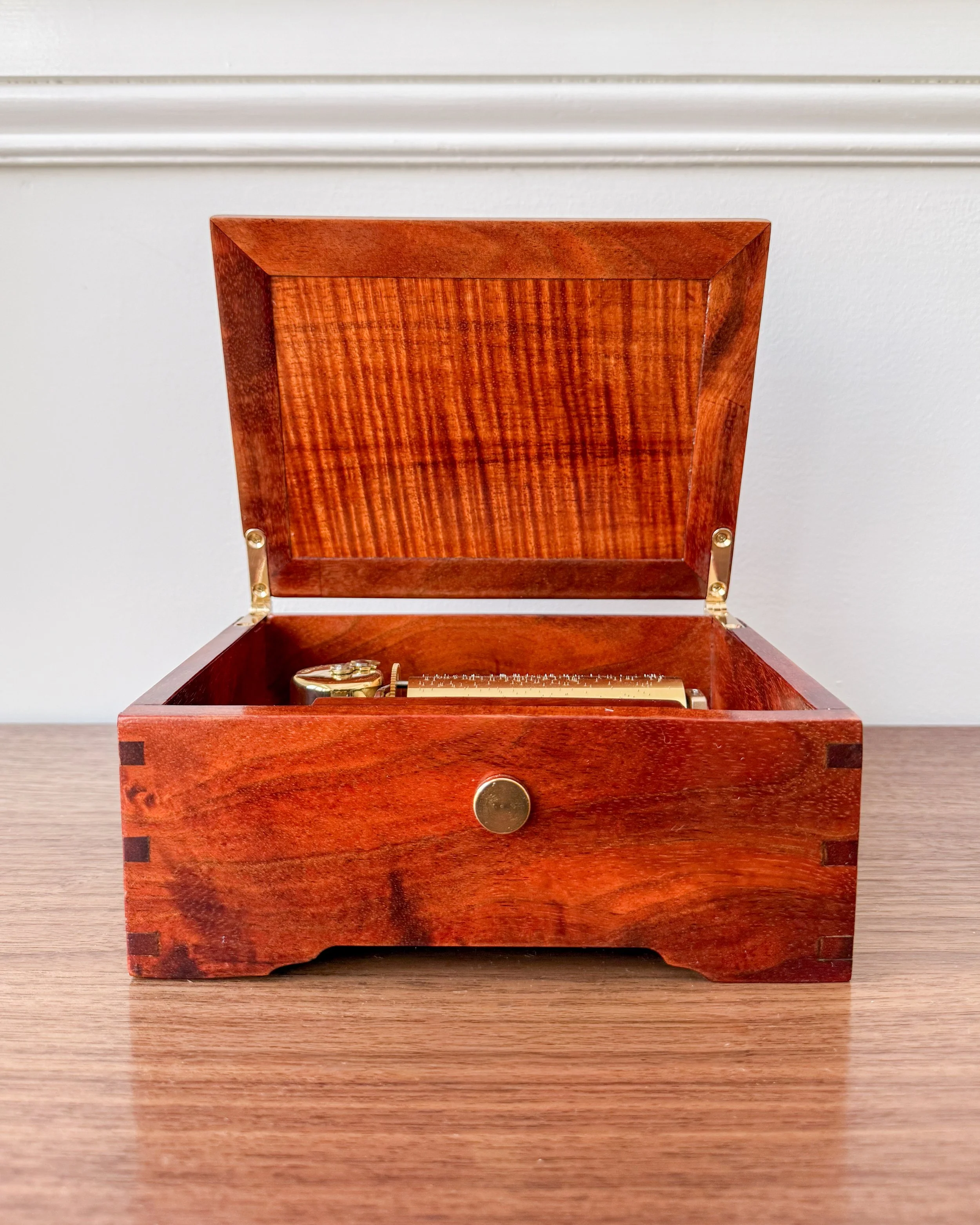 A vintage wooden box with a hinged lid, containing a brass timer and other small items, placed on a wooden surface.