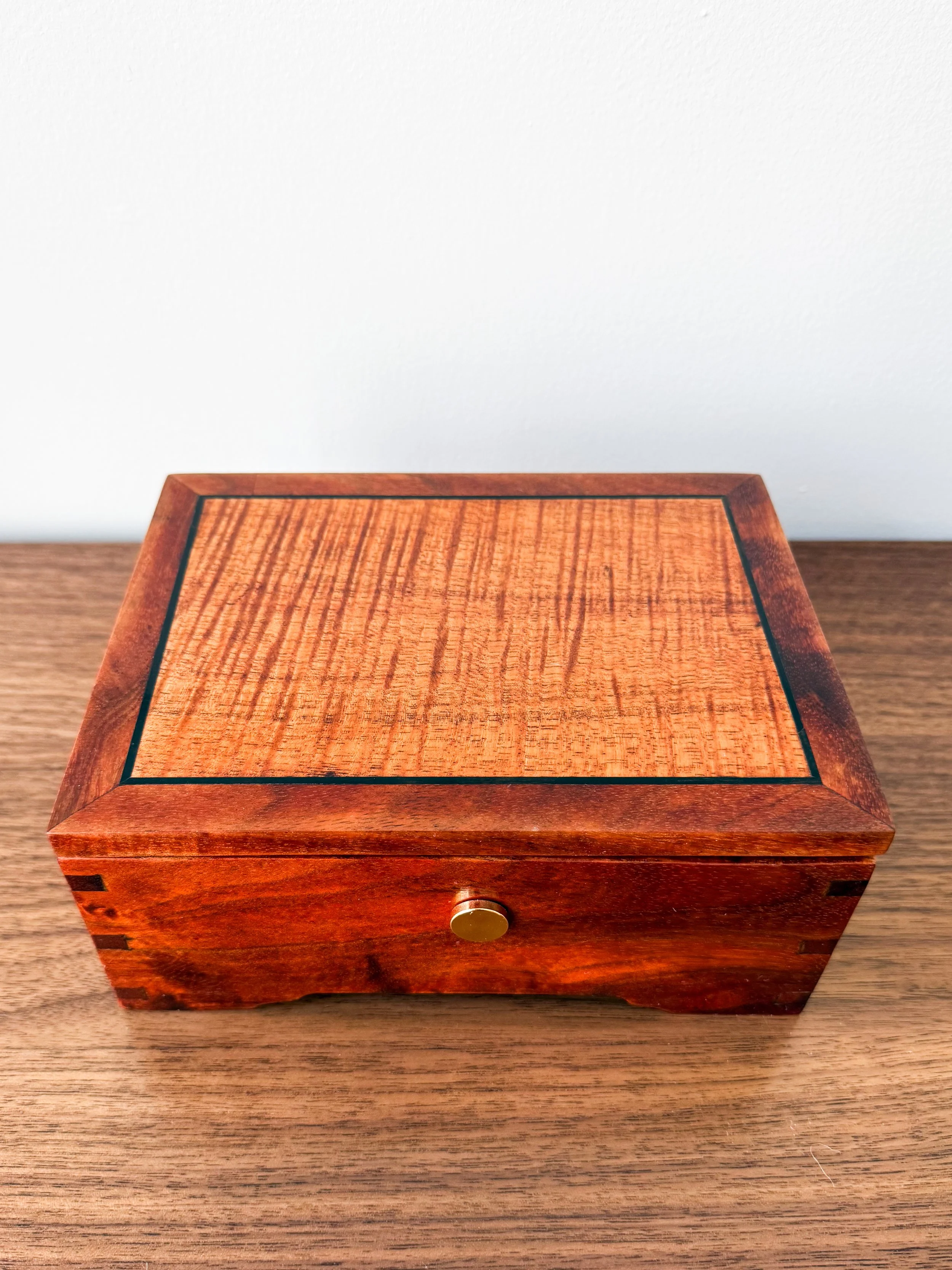 A square wooden box with a small brass knob on the front, placed on a wooden surface against a plain white background.