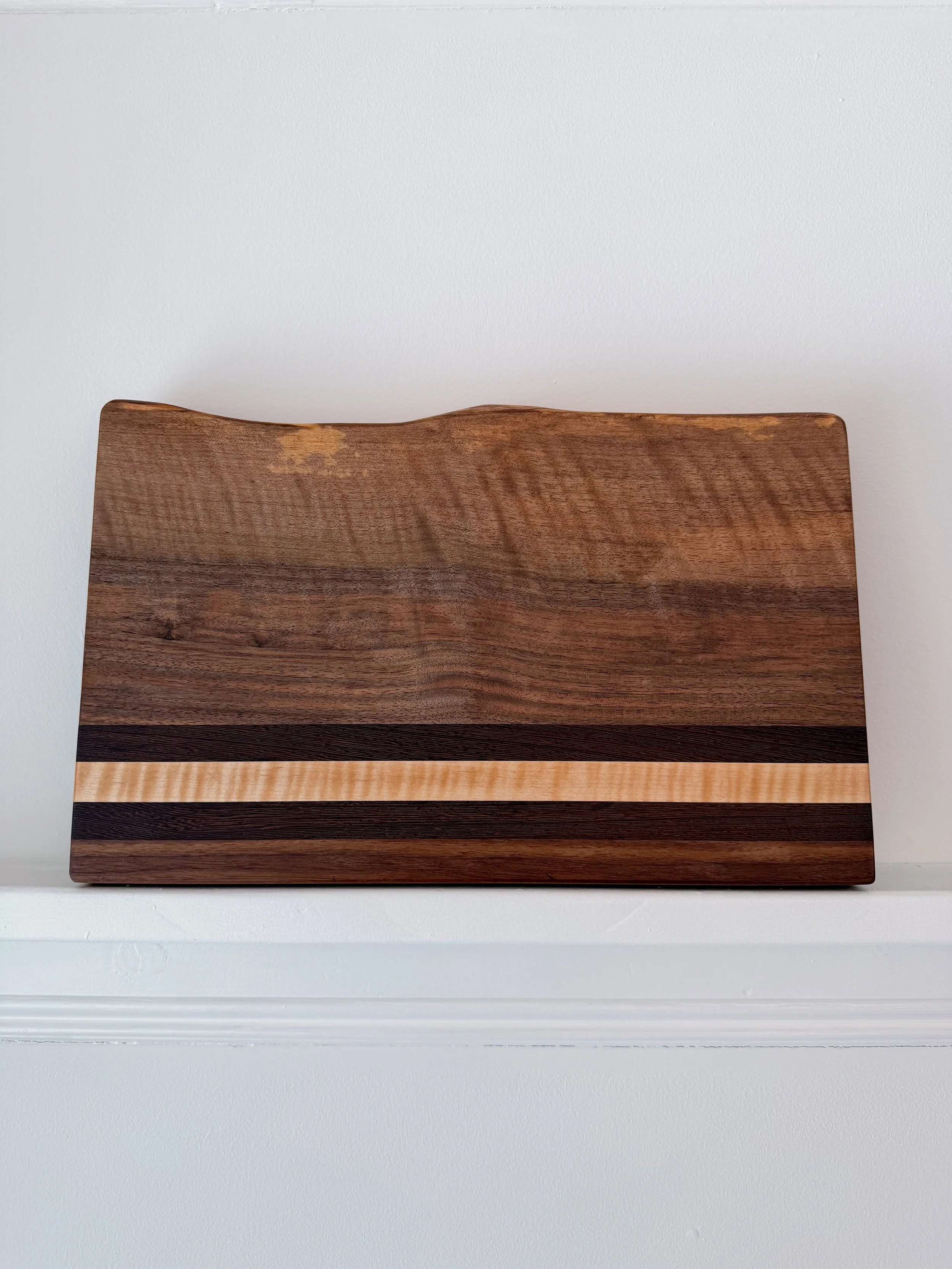 Close-up of a rectangular wooden cutting board with a natural wood grain pattern, placed against a white wall.