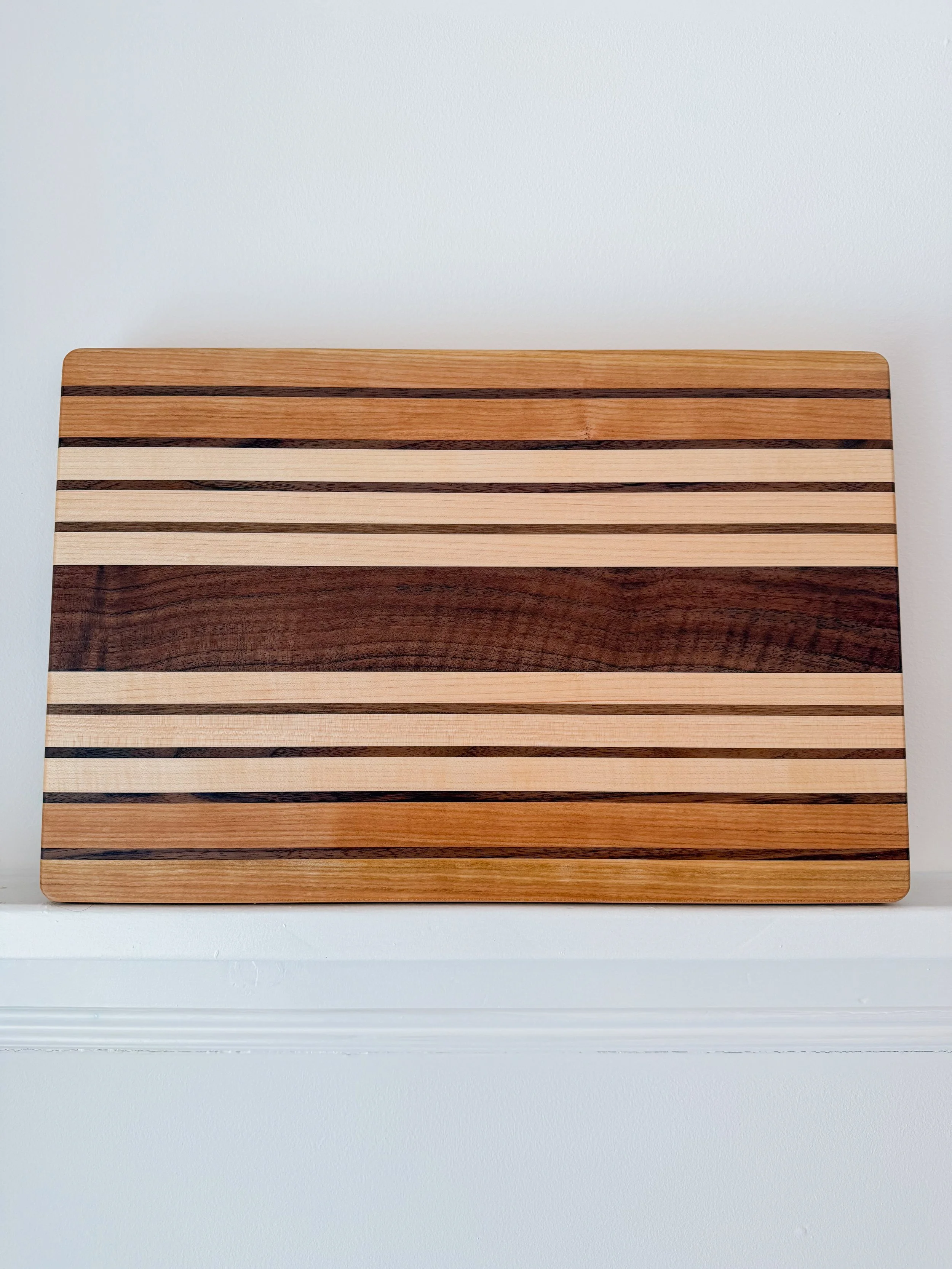 A wooden cutting board with horizontal stripes in different shades of brown and natural wood, placed on a white surface.