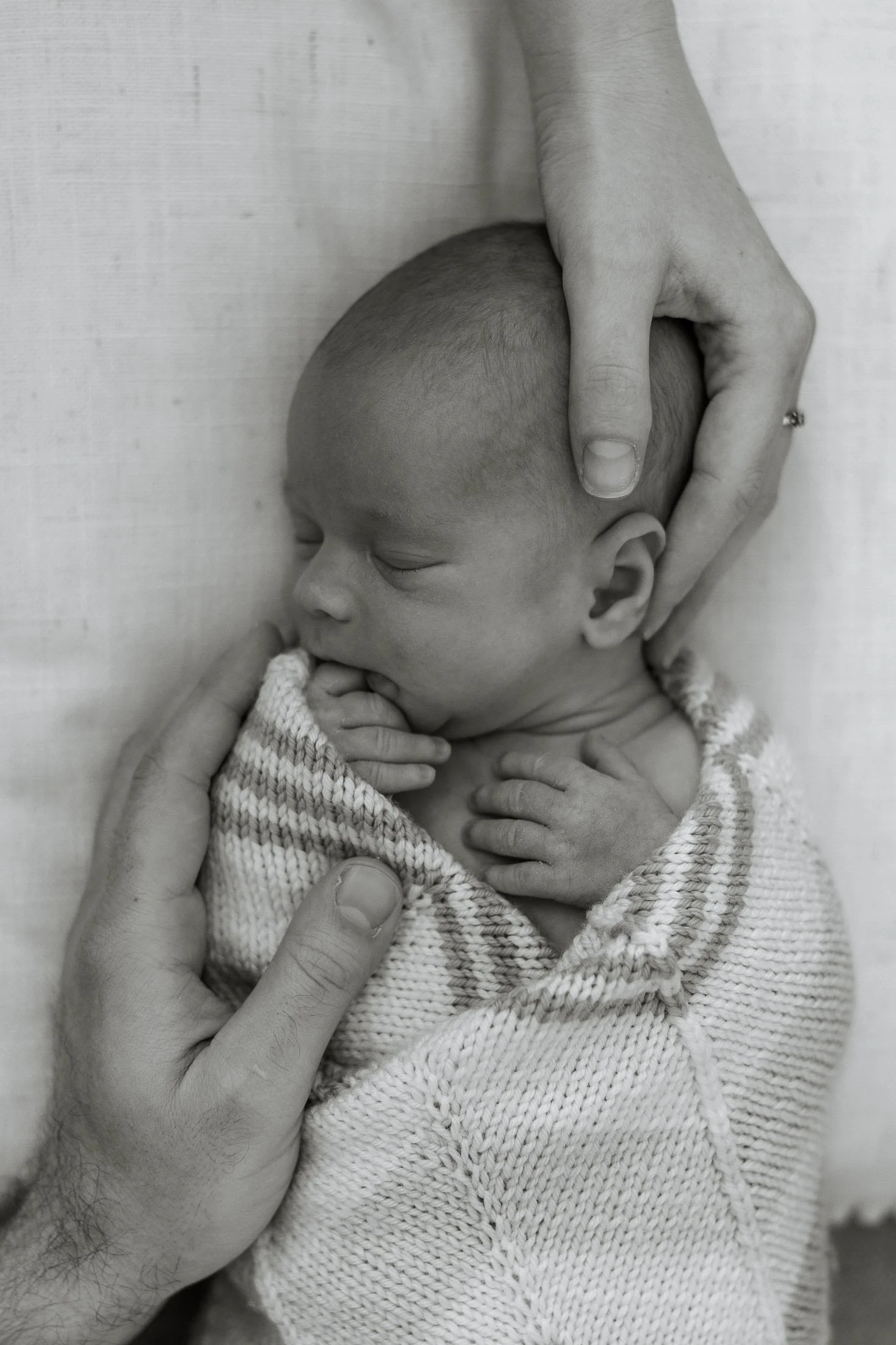 Black and white photo of a sleeping newborn baby being gently cradled by an adult's hands.