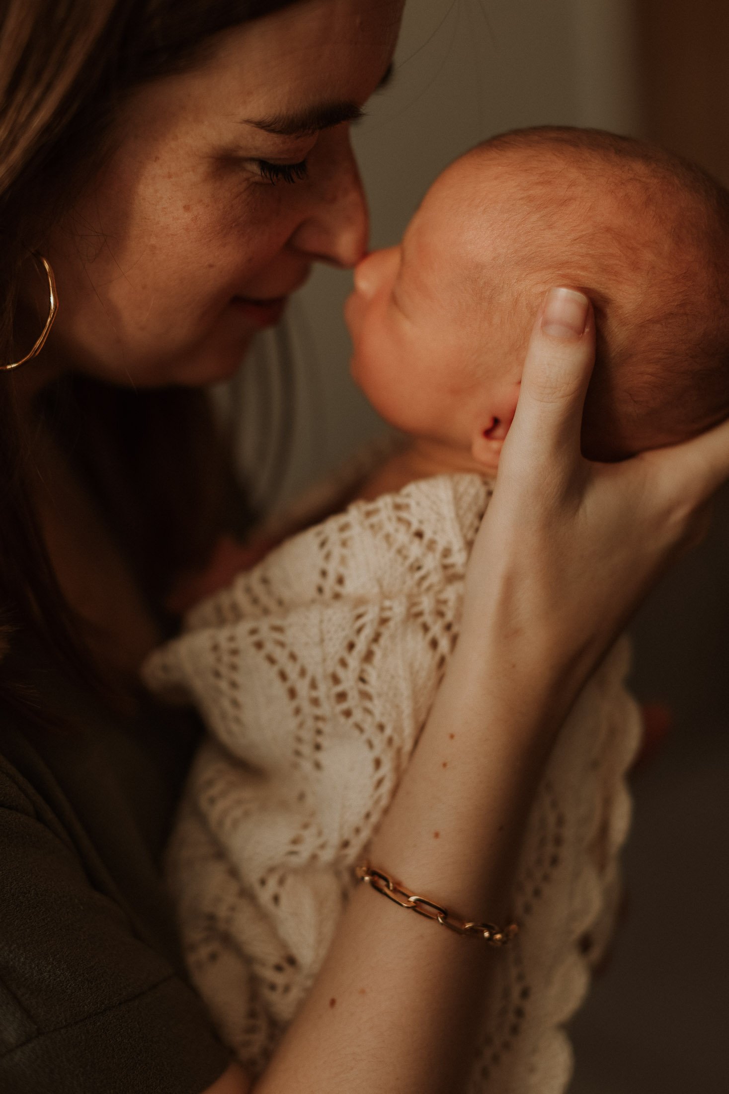 A woman gently holds a newborn baby close to her face, touching their foreheads together in a tender moment.