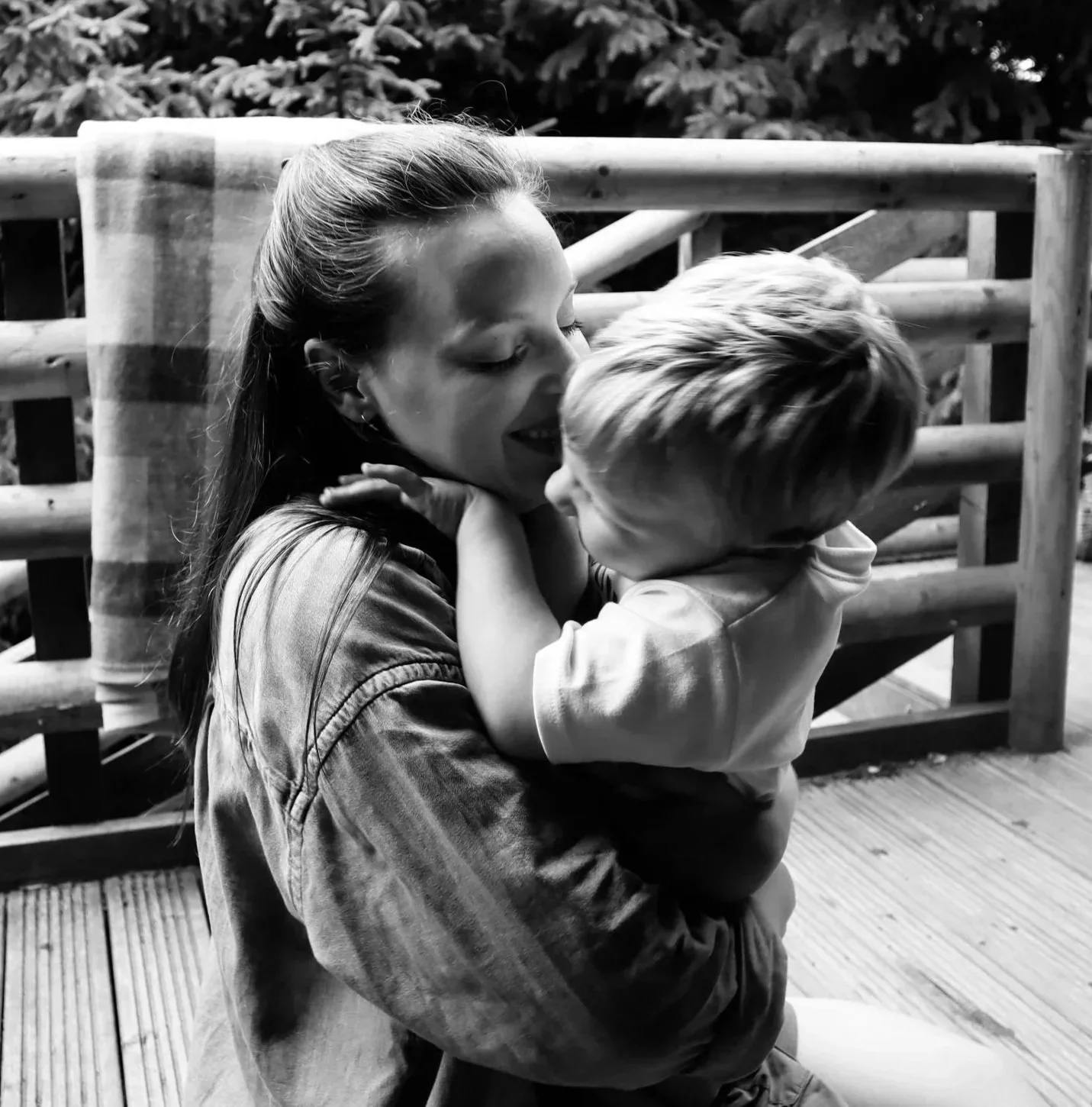 A woman and a young boy sharing a joyful moment outside on a wooden deck, with the woman holding the boy close and both smiling in London.