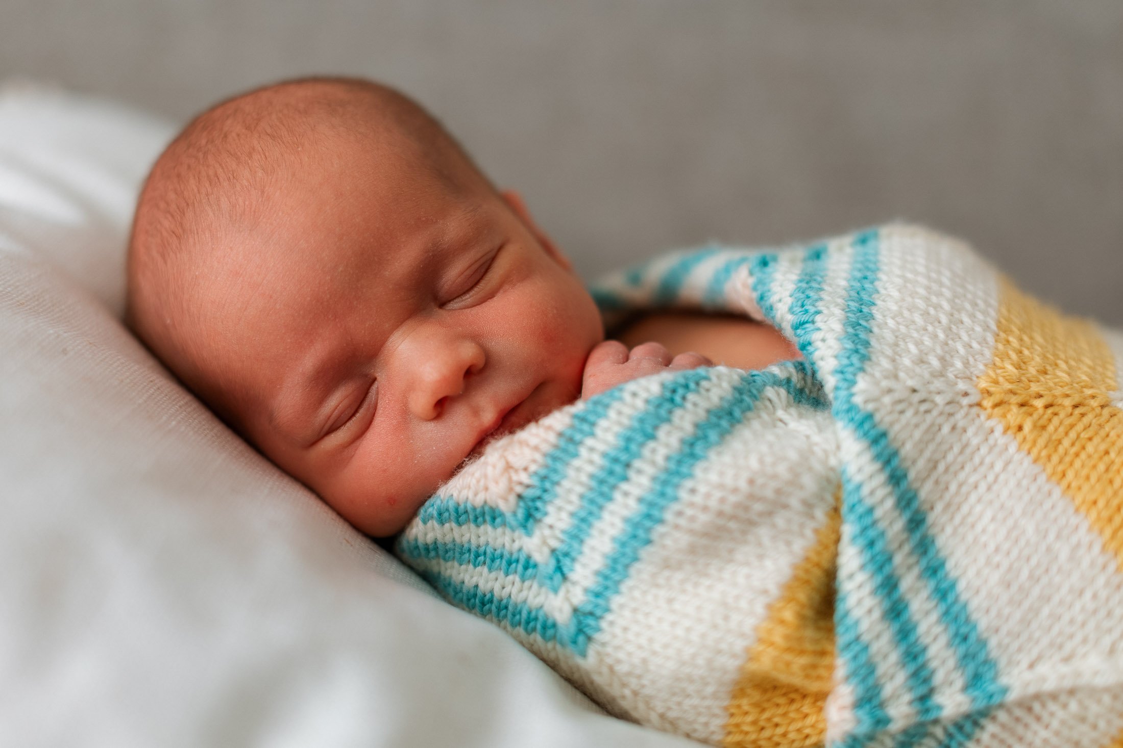 A sleeping newborn baby wrapped in a striped blanket, resting on a soft surface.