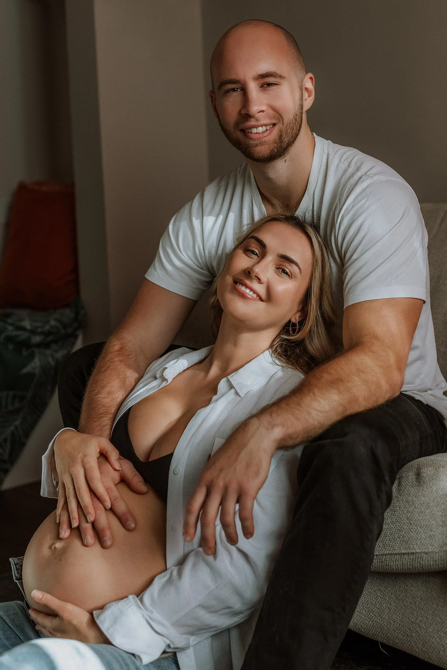 couple in living room in Surrey home, both with hands on baby bump, smiling at camera