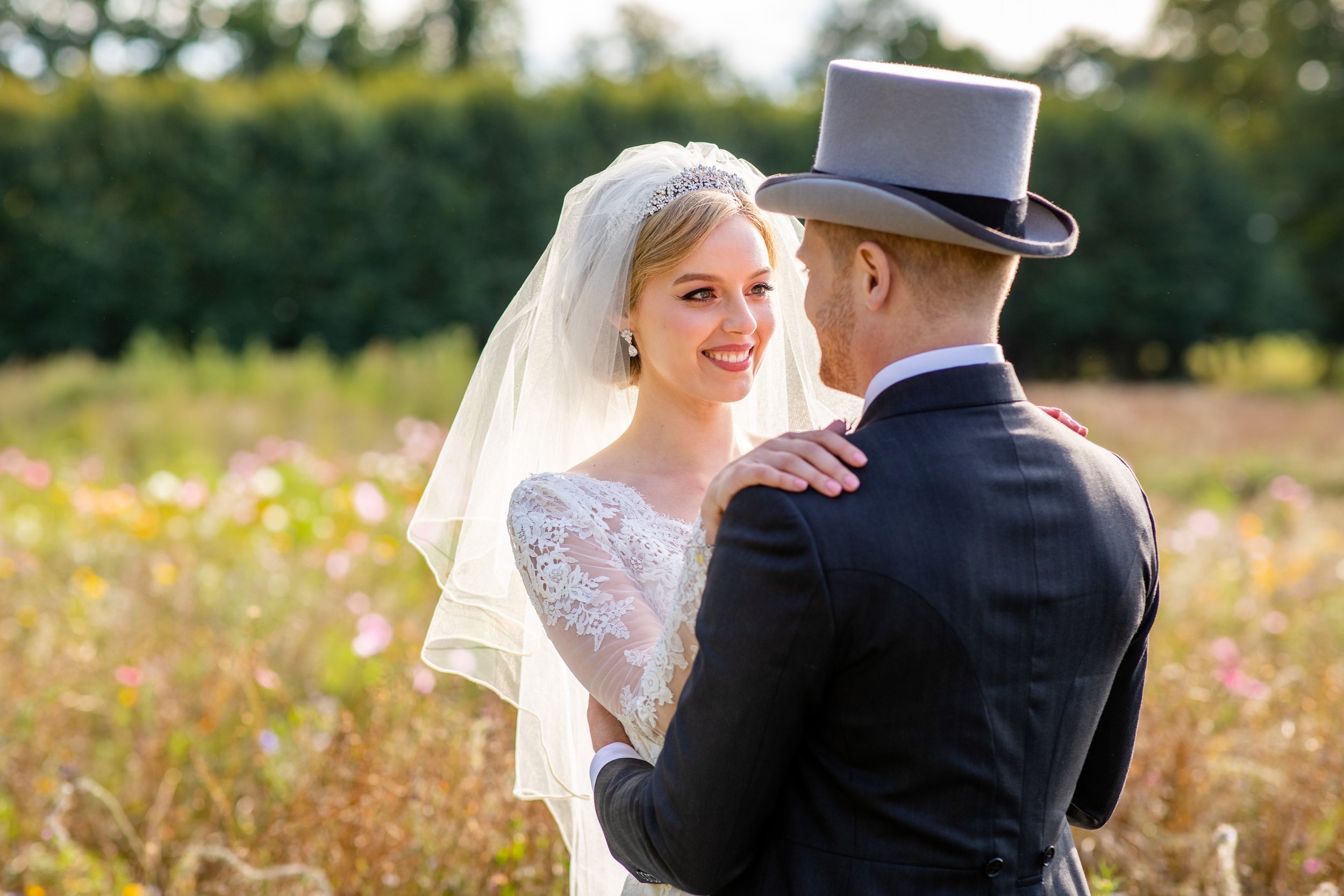 A bride and groom celebrate their wedding outdoors in a field of wildflowers on a sunny day, gazing into each other's eyes.