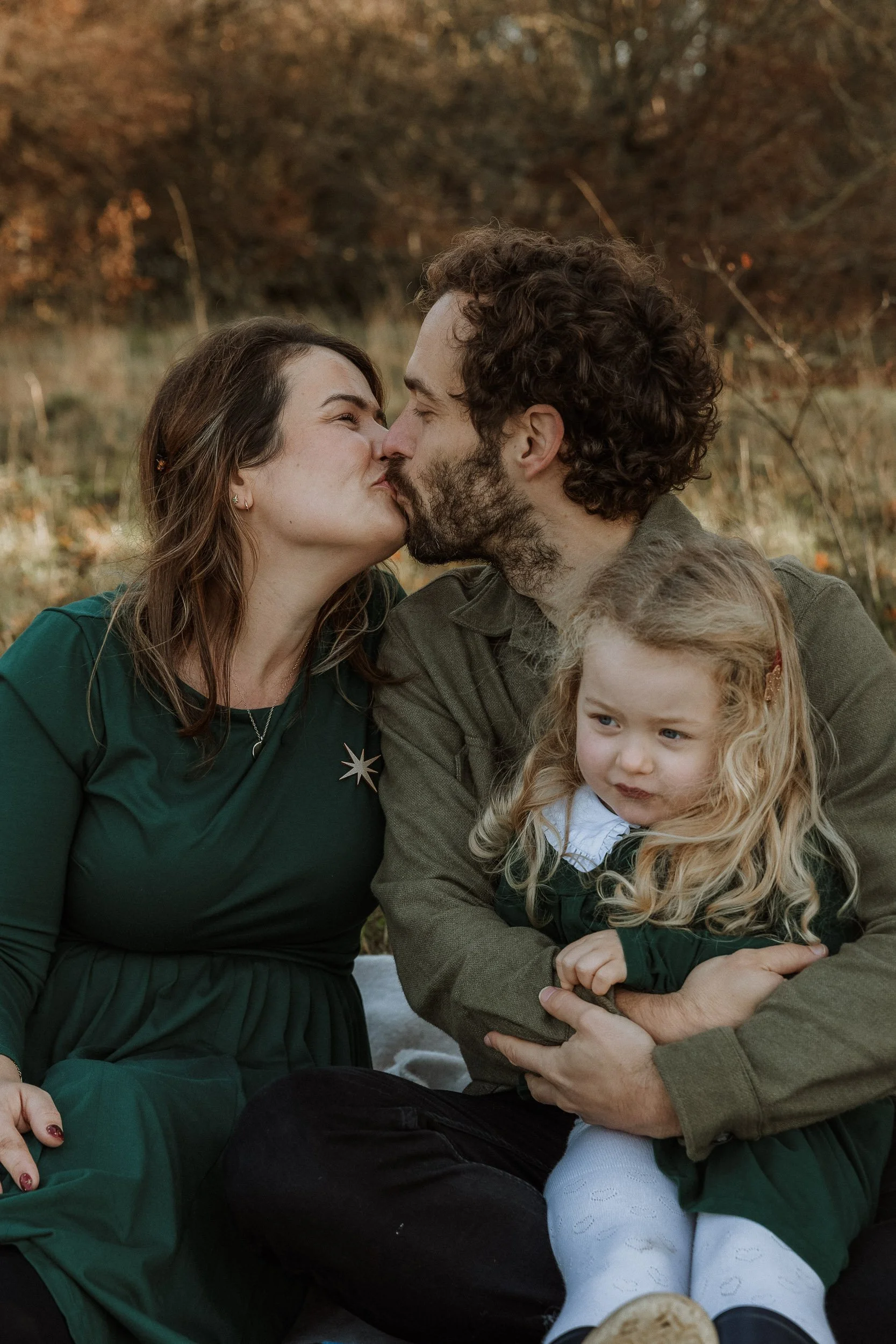 Outdoor family photo of parents and little girl in Surrey park in autumn