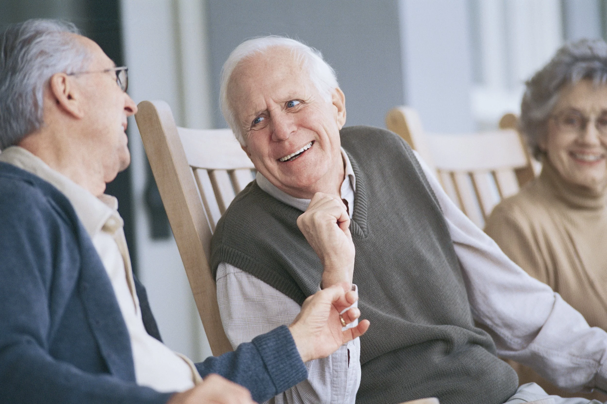 Groupe de personnes âgées assises en cercle, discutant et souriant, dans une salle lumineuse.