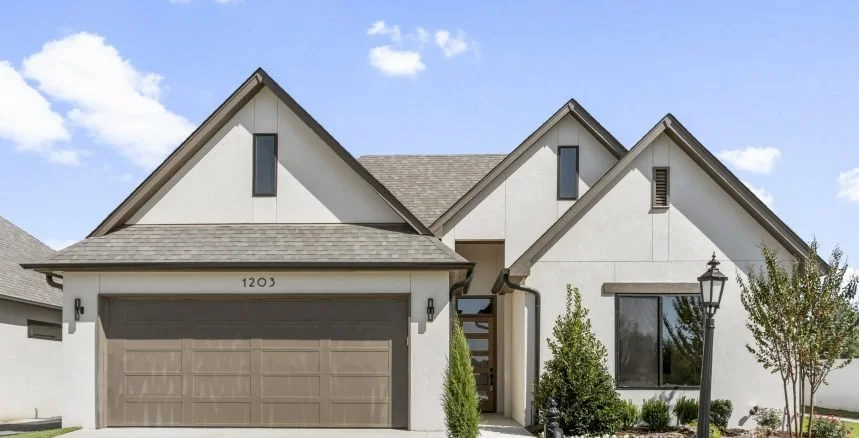 Modern suburban house with white exterior, gray roof, two-story design, large front window, and a two-car garage, with a lamp post and landscaped yard.