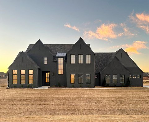 Large black house with multiple gabled roofs and illuminated windows under a partly cloudy sky.