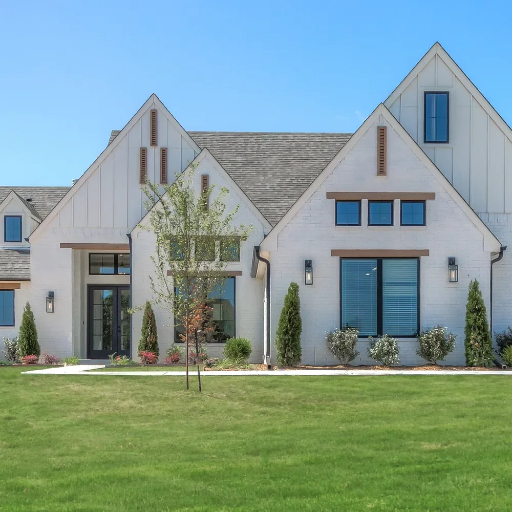 Modern white house with large windows, a manicured front yard, and a tree in front on a clear day.