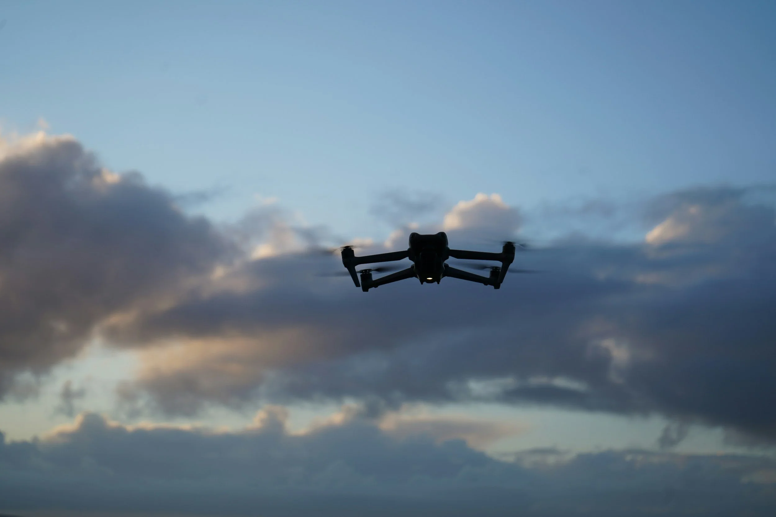 A drone flying in the sky with clouds during dusk or dawn.